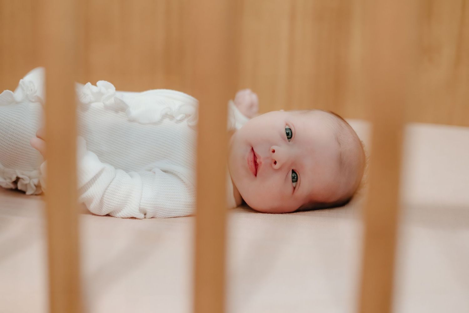 Side view of baby lying in wooden crib with white bedding.