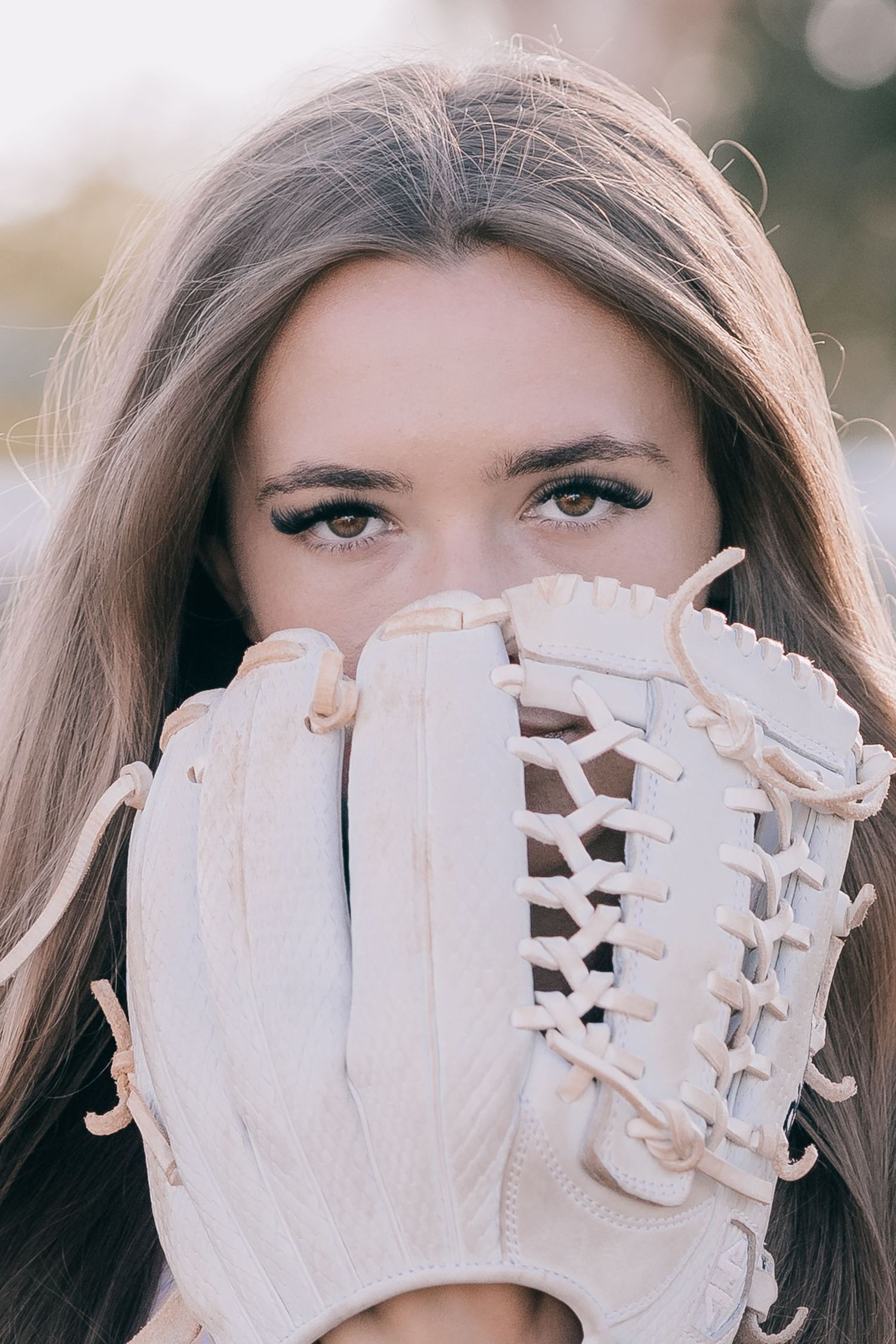 A creative portrait showing a baseball glove held up against soft natural lighting.