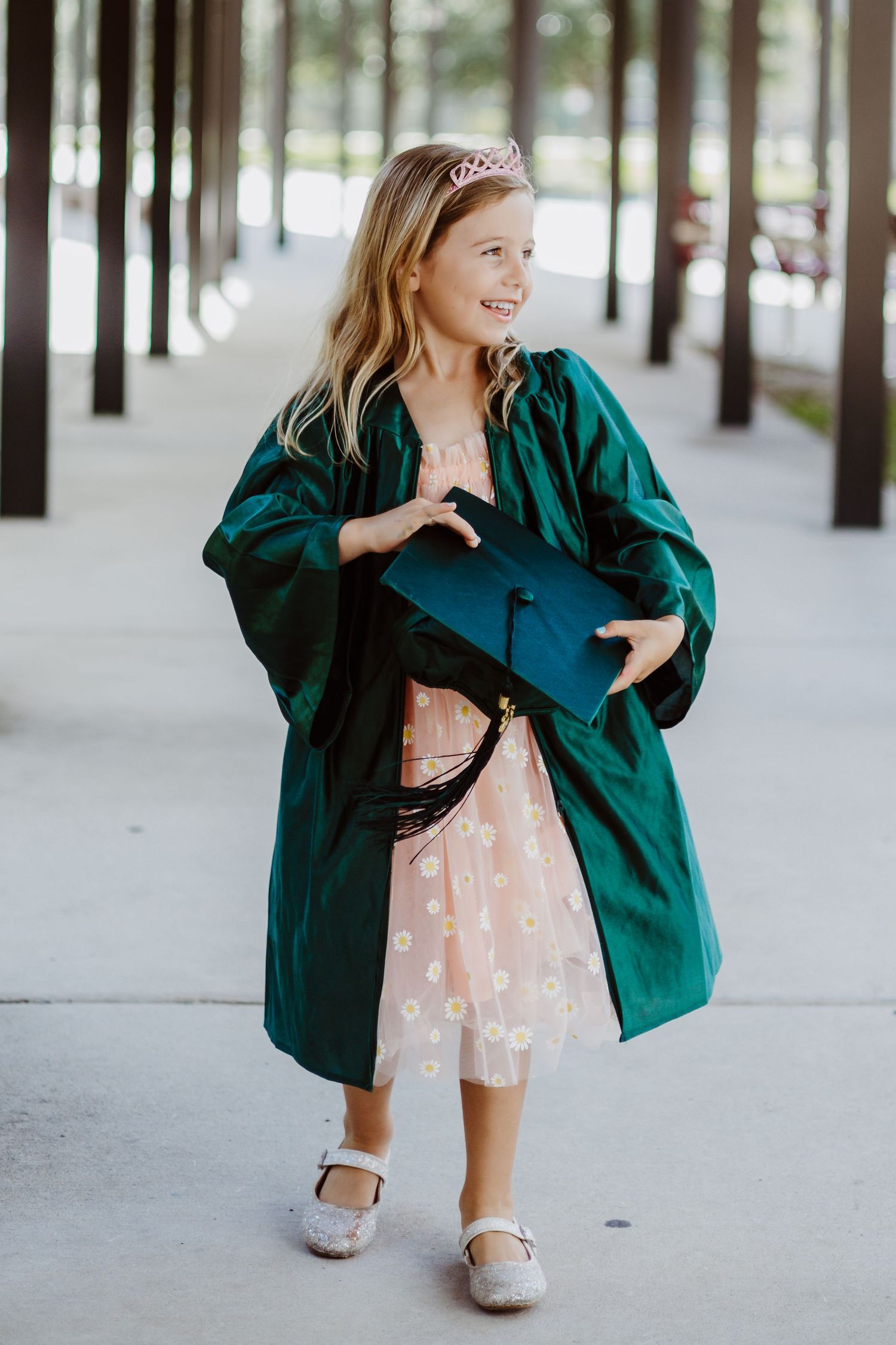 Person in emerald green jacket and floral dress poses playfully in a snowy forest setting with white trees.
