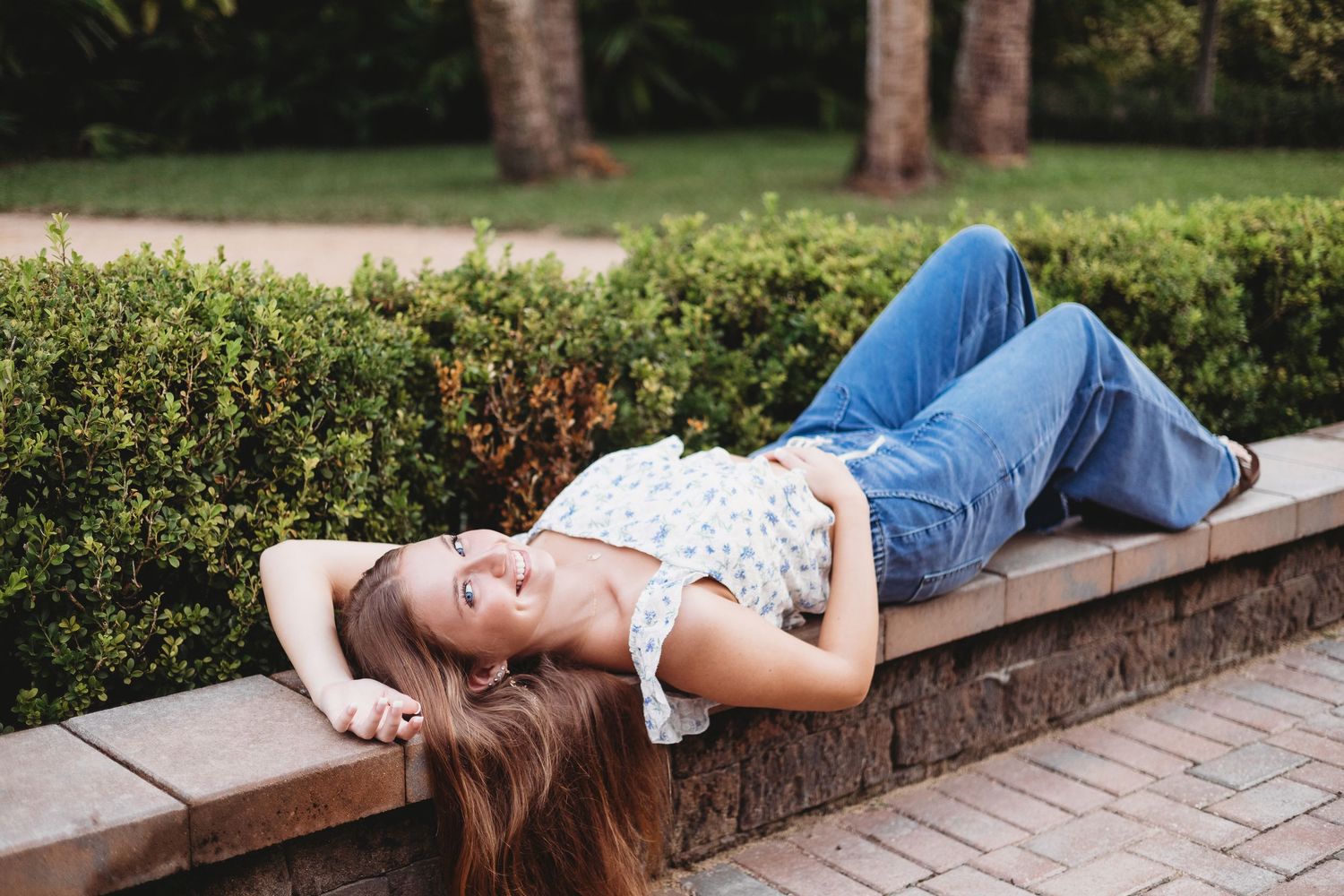 Someone relaxes on a stone wall in a garden setting surrounded by lush greenery.