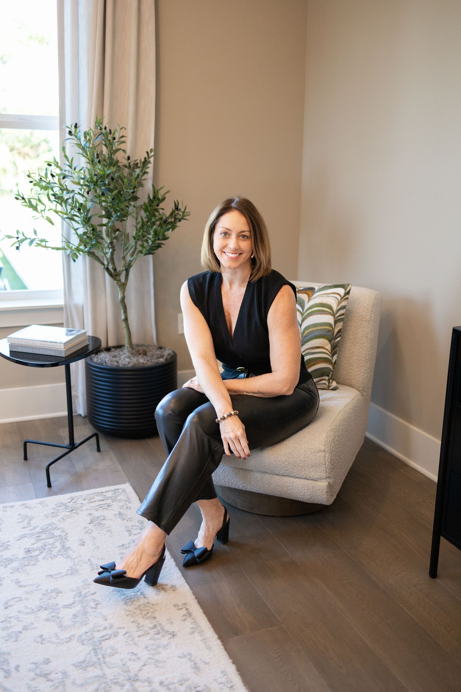 A person sits in a modern gray armchair against a beige wall with hardwood floors and minimalist decor.