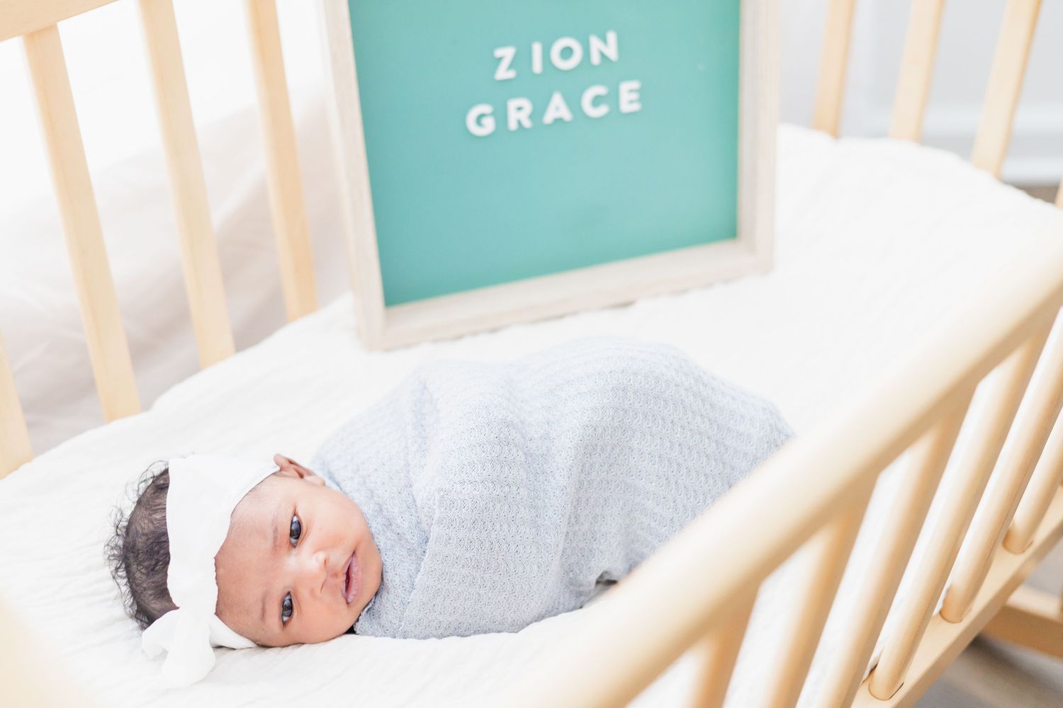 Baby lying in wooden crib with turquoise decor and white bedding.
