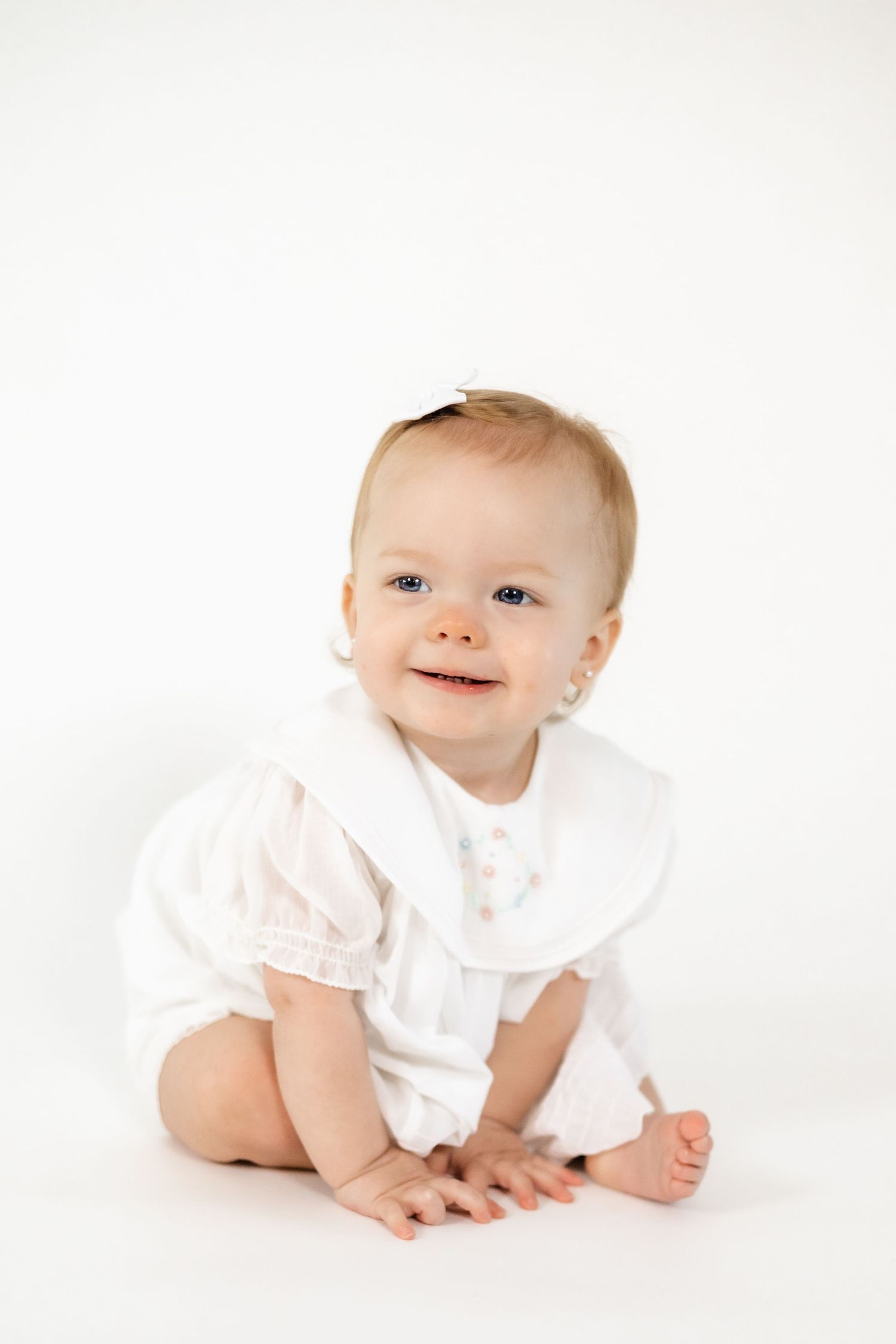 Baby wearing white ruffled outfit lying on white background smiling and crawling.