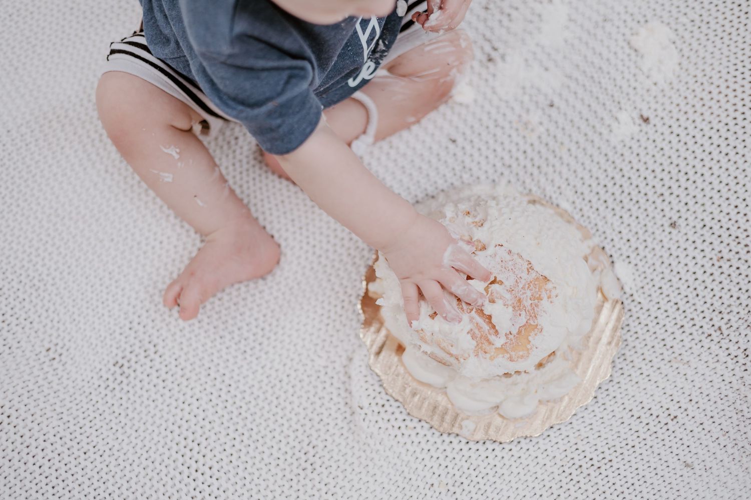 Small hands reach for a cream-covered dessert on a textured gray surface.
