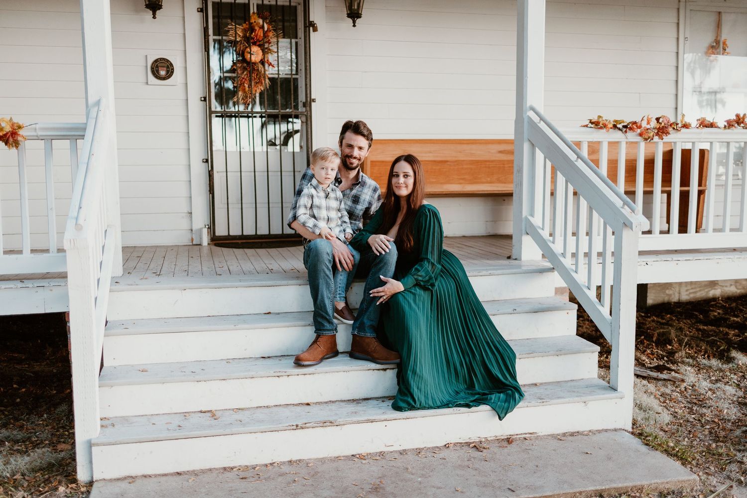 A couple sits together on white porch steps decorated with autumn pumpkins and fall decor.