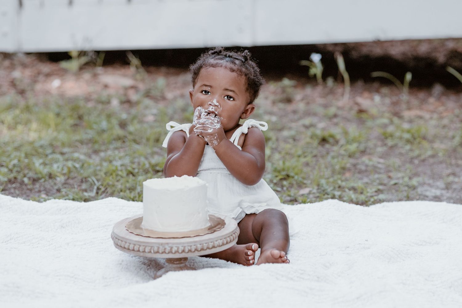 Baby plays with cake during first birthday cake smash photo session on white backdrop.