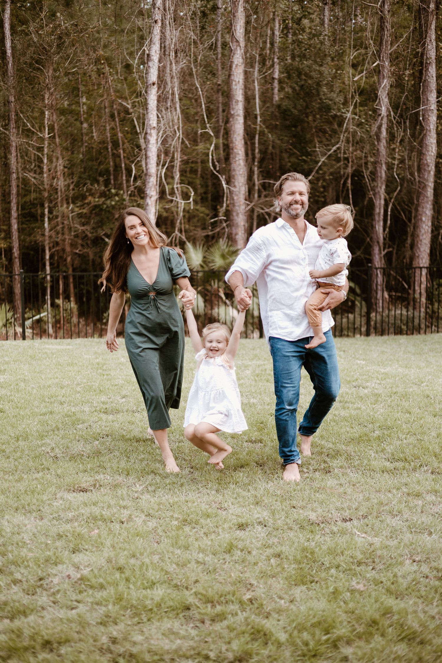 Family playing and running together on grassy field with forest backdrop.