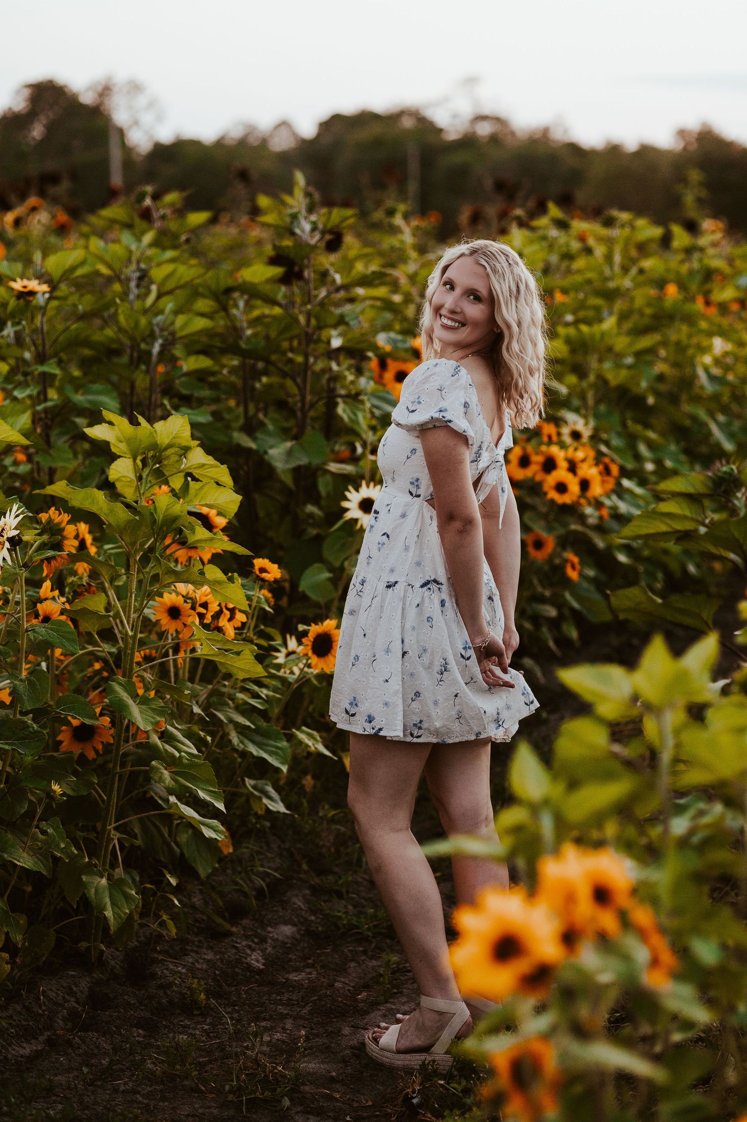 Person in a floral dress standing in a vibrant sunflower field at golden hour.