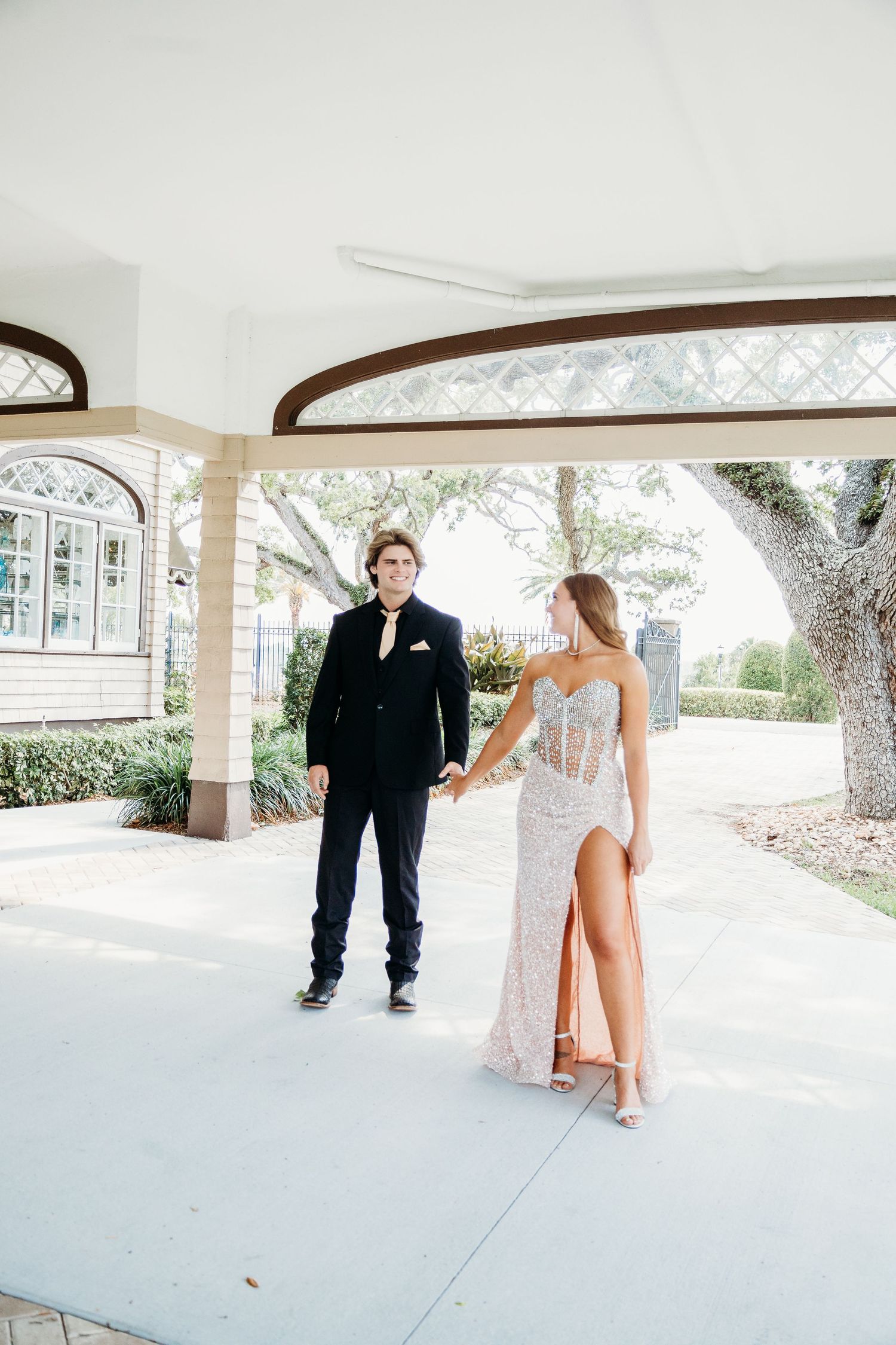A couple stands together on a white concrete patio during what appears to be a special occasion.