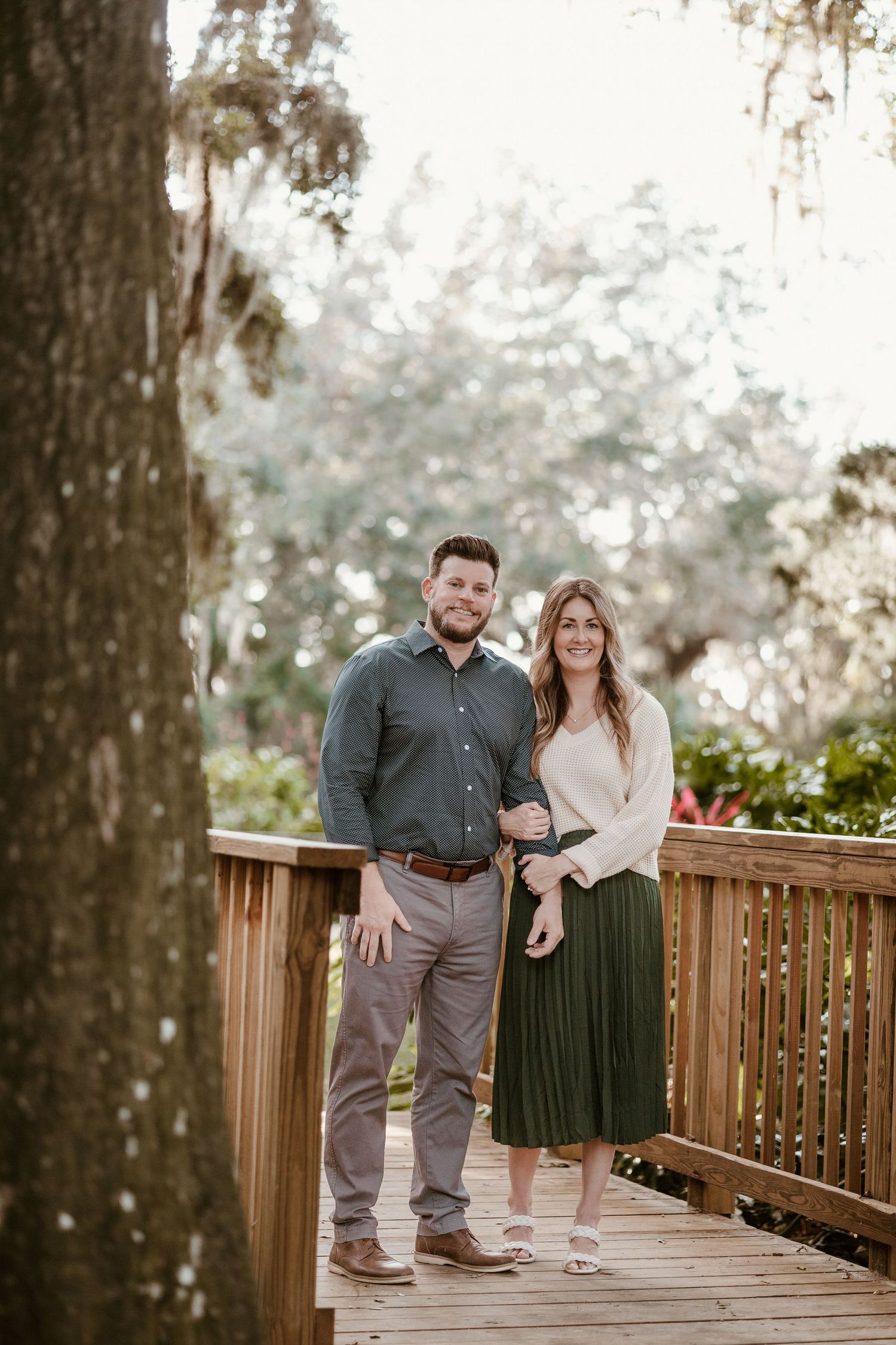 Couple poses together on wooden boardwalk surrounded by tall trees.