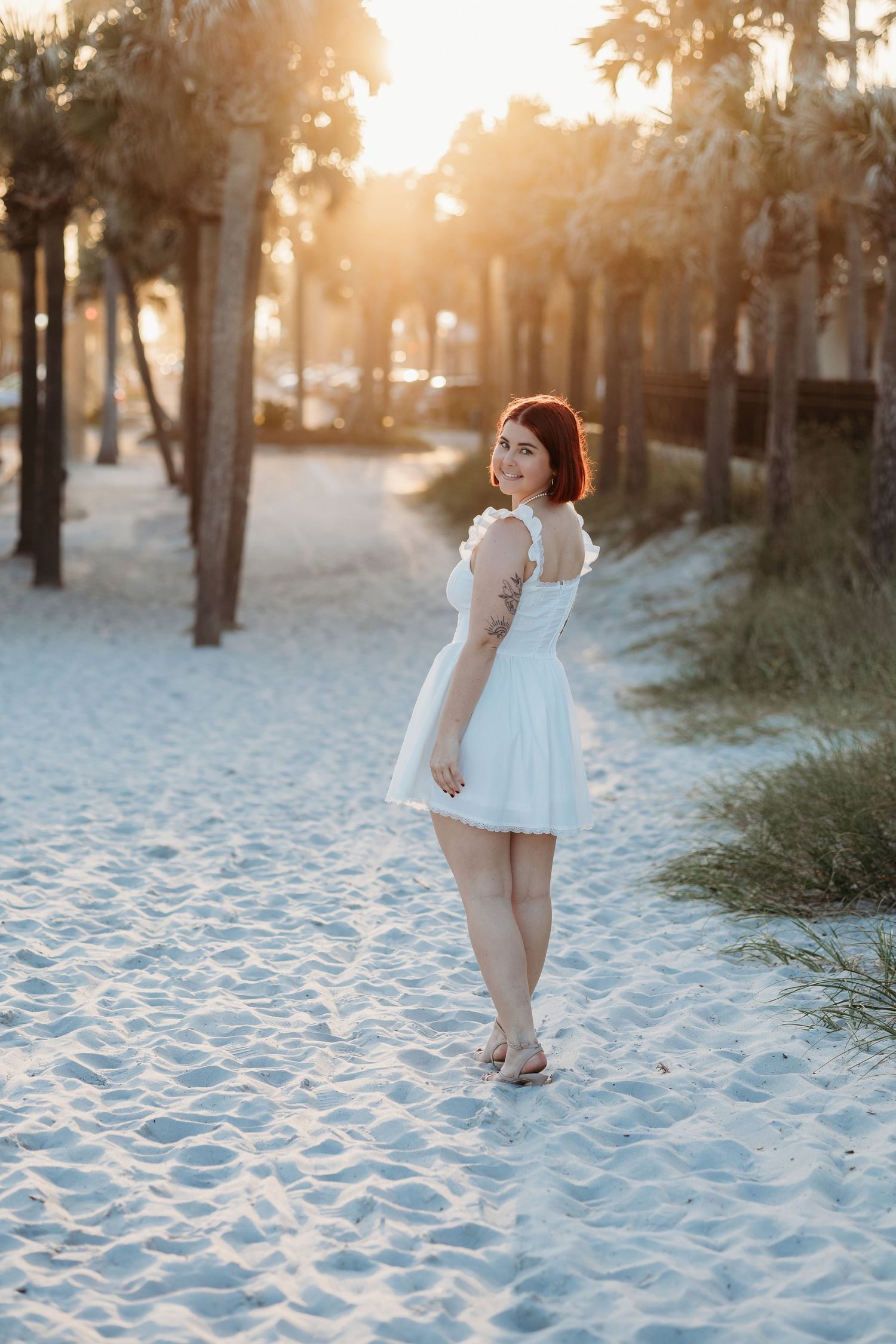 Sunset beach photoshoot with white dress against palm trees and sandy backdrop.