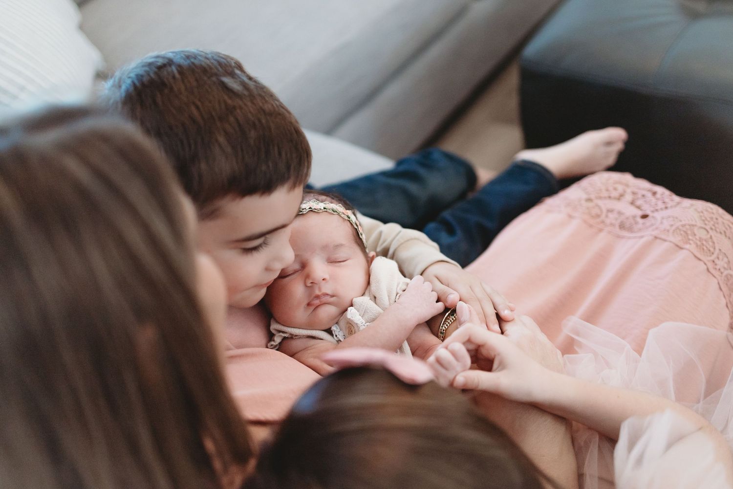 Parent gently kissing sleeping newborn baby wrapped in soft pink blanket during lifestyle photography session.