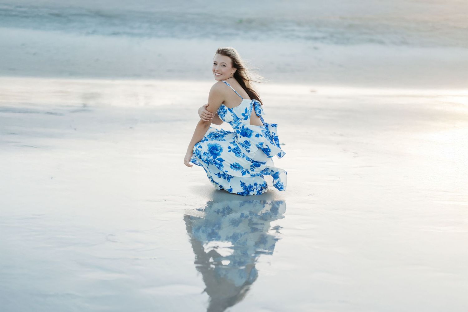 Artistic water reflection photos in a blue floral dress at the ocean's edge.