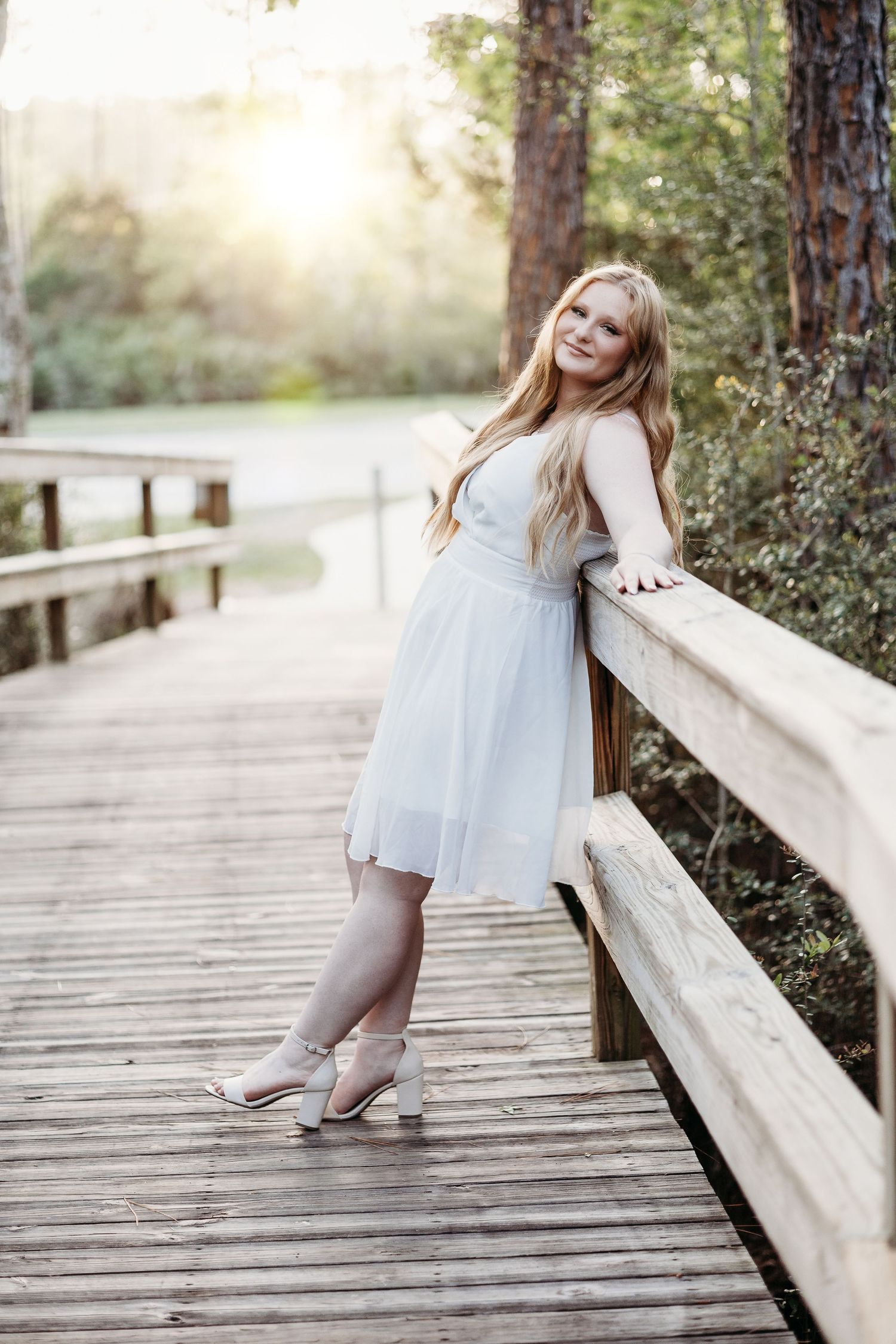 Person in white dress posing on wooden boardwalk in natural setting.