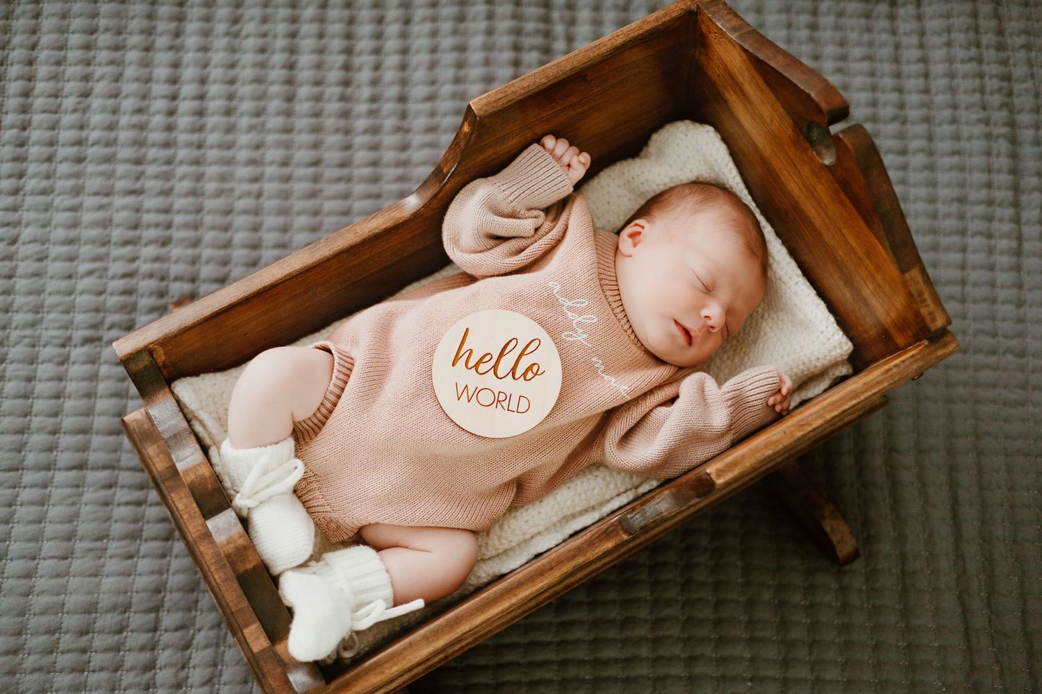 A sleeping newborn rests in a rustic wooden box with soft white padding.