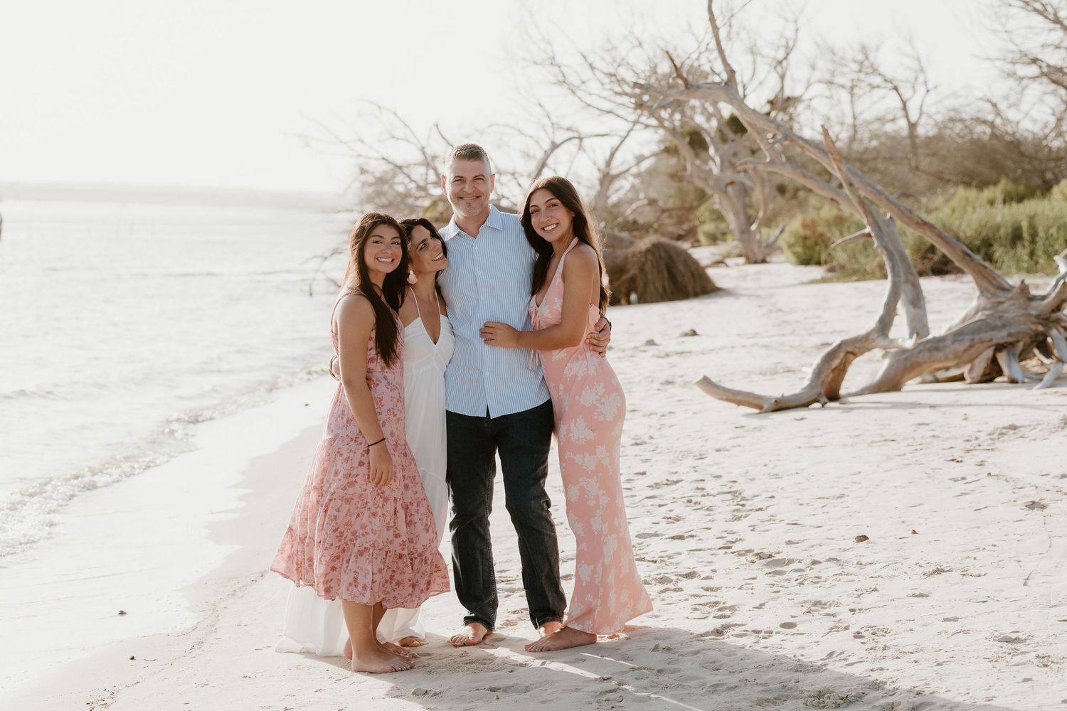 Family portrait session on a white sandy beach with driftwood and natural scenery.