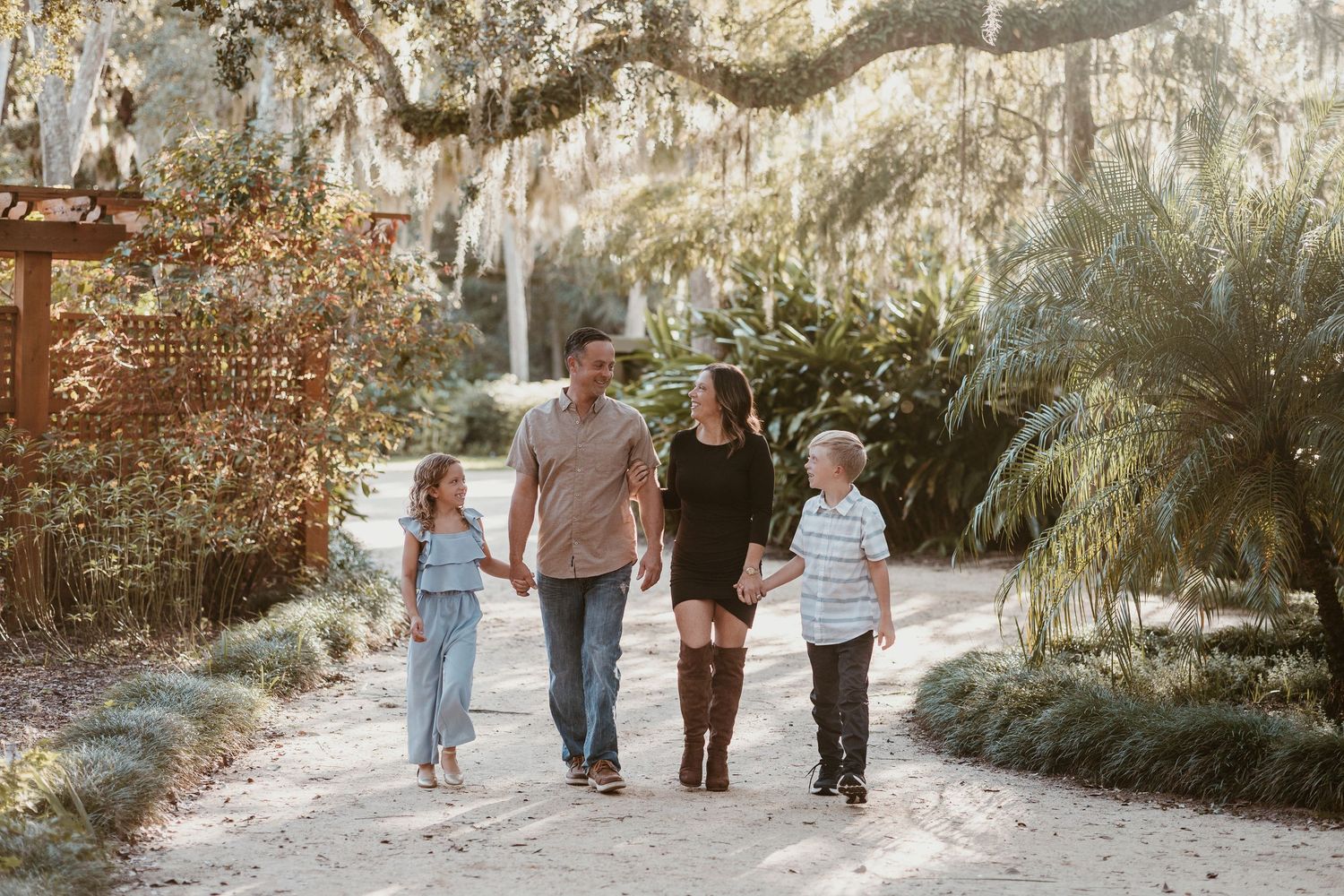 A group walks together down a scenic path lined with Spanish moss and palm trees on a sunny afternoon.
