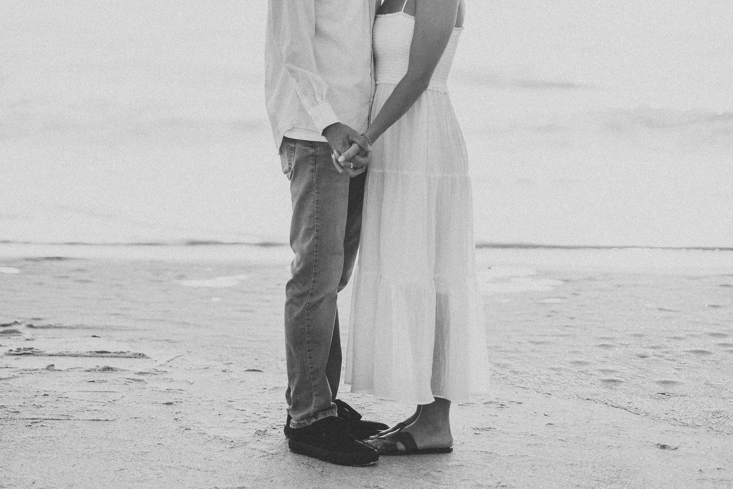 Black and white photos of a couple embracing on a sandy beach.