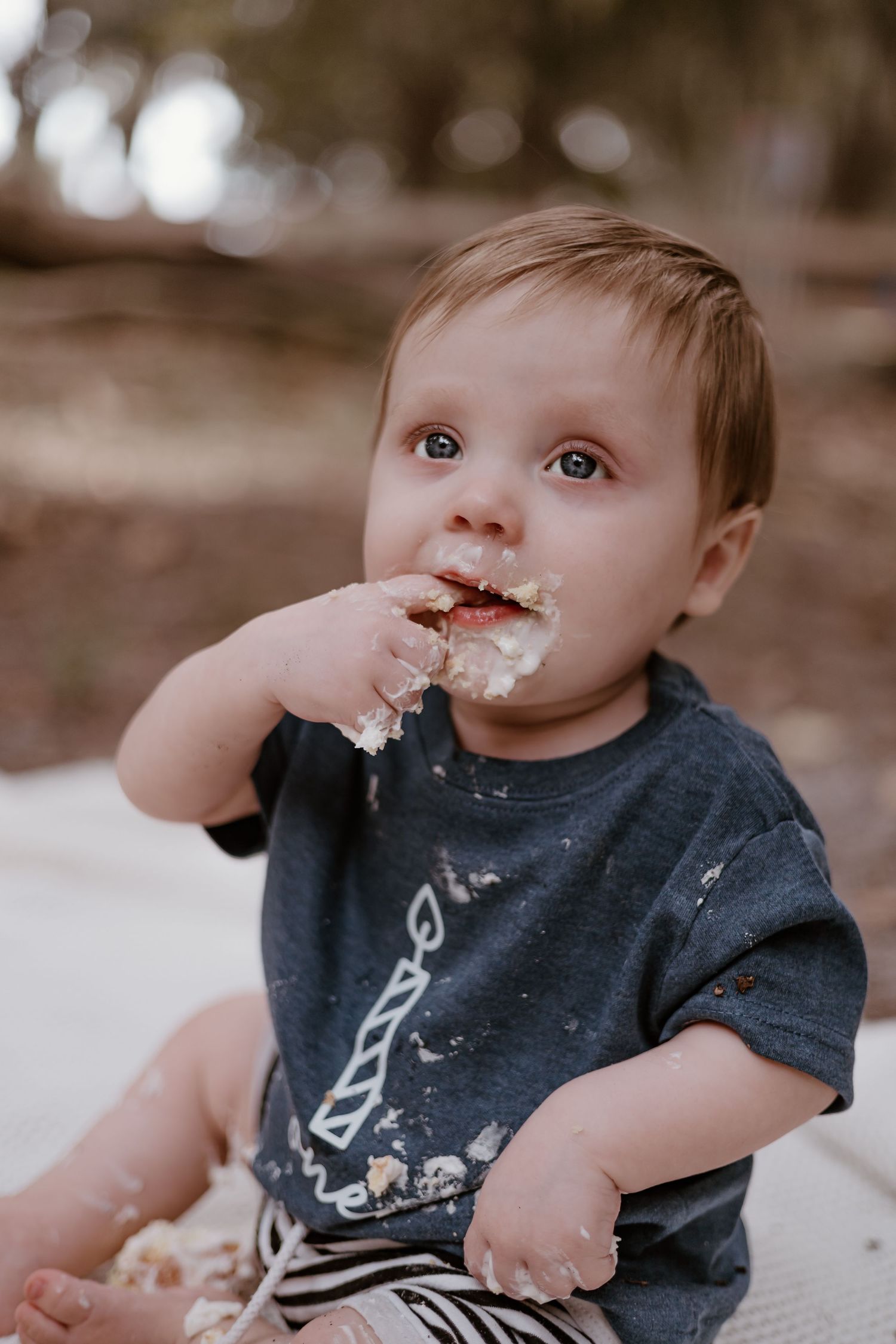 Baby in navy shirt enjoying messy cake smash with white frosting.