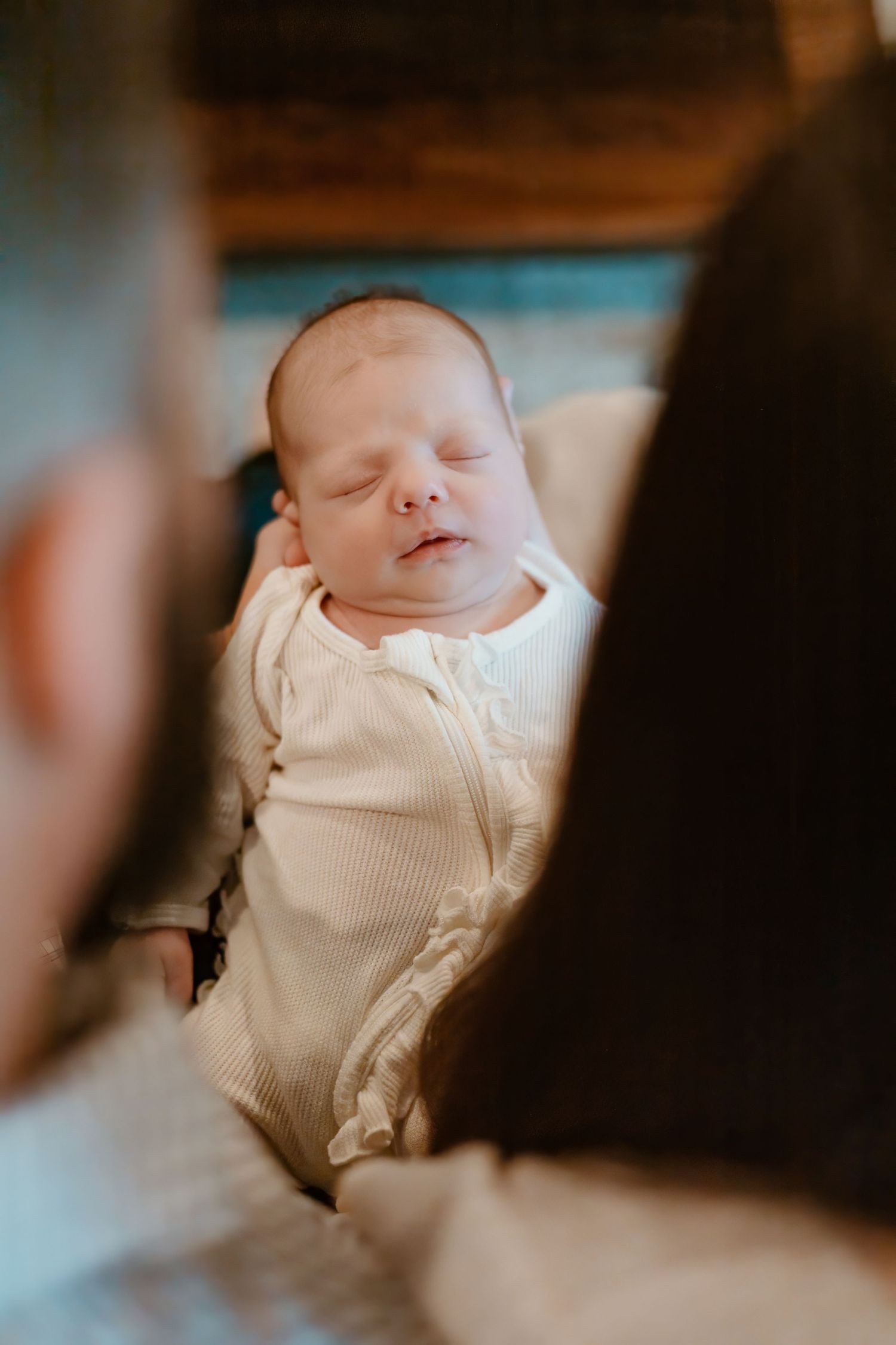 A sleeping newborn in white clothing is held gently against a dark background.