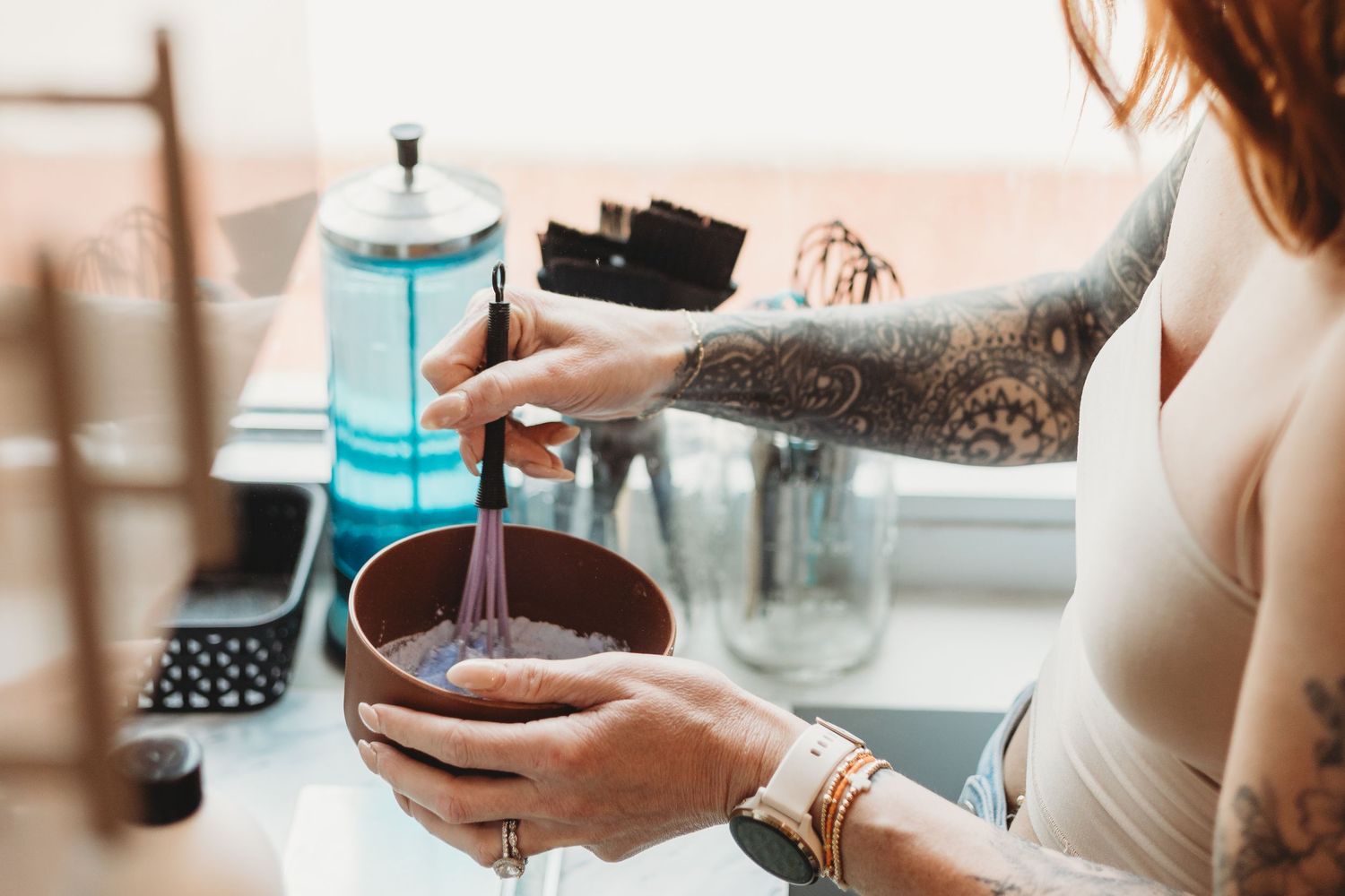 Close-up of hands preparing coffee drinks with turquoise mugs on wooden surface.