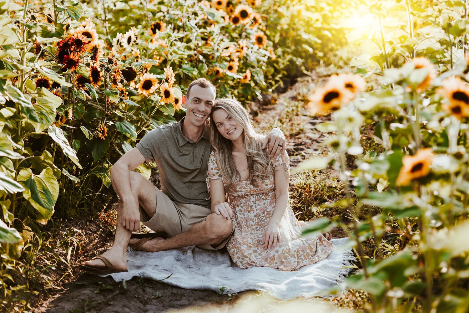 A couple sits on a blanket in a sunflower field during golden hour.