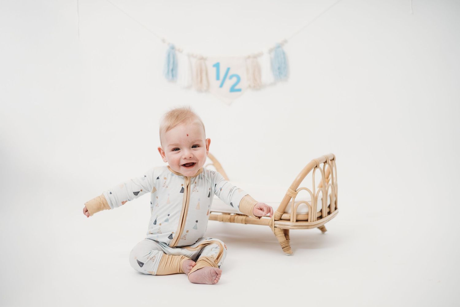 Baby in white onesie lying on floor with blue decorative banner overhead.
