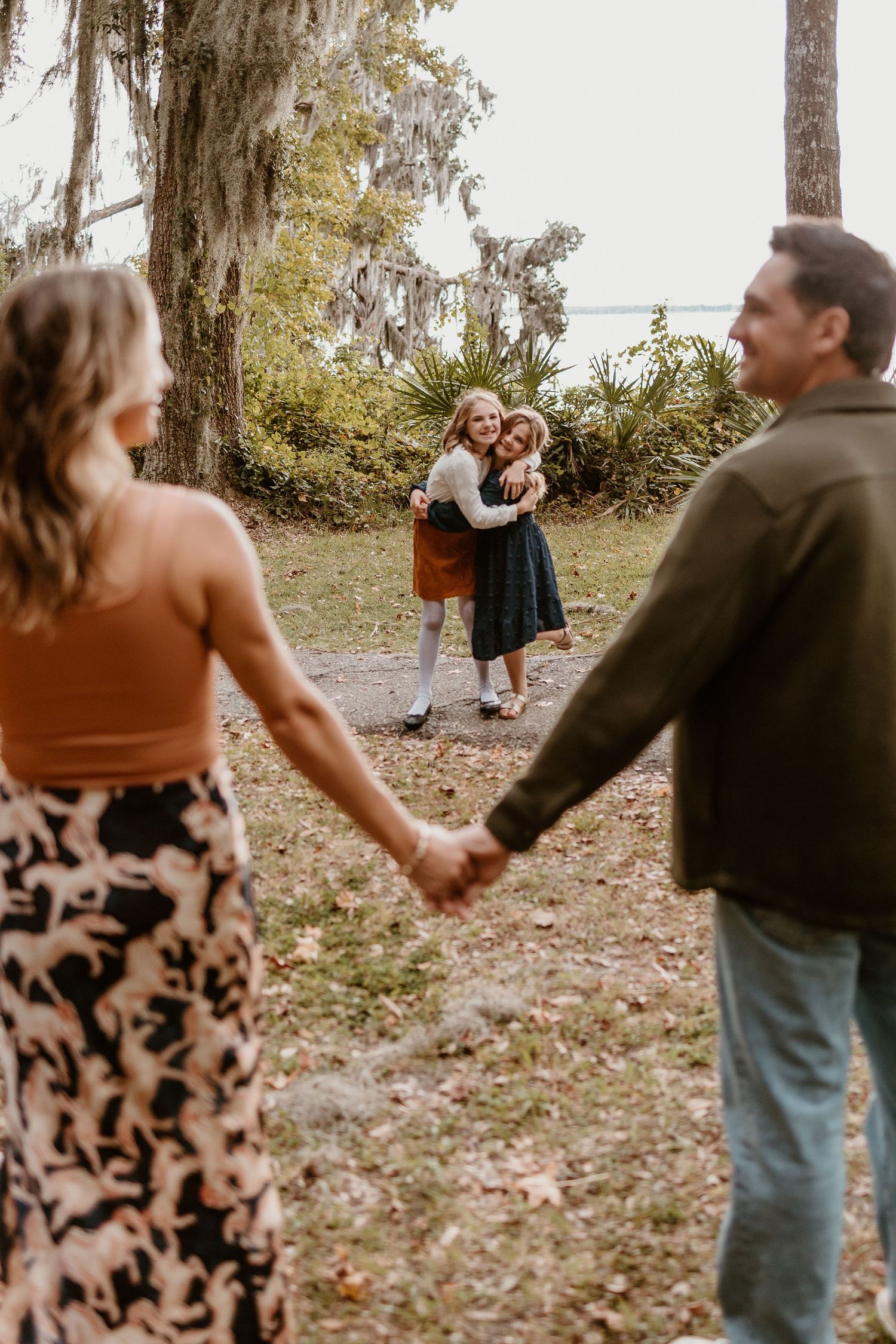 Two couples share a romantic moment in a scenic outdoor setting with Spanish moss draped trees and natural lighting.