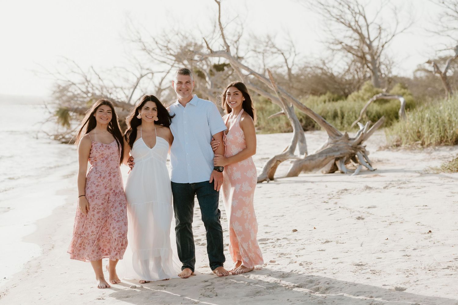 Family portrait session on sandy beach with driftwood and natural coastal scenery.