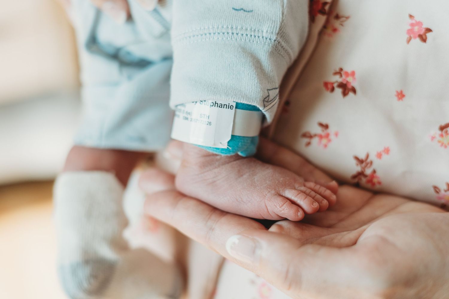 Close-up of gentle hands holding a baby in soft blue clothing.