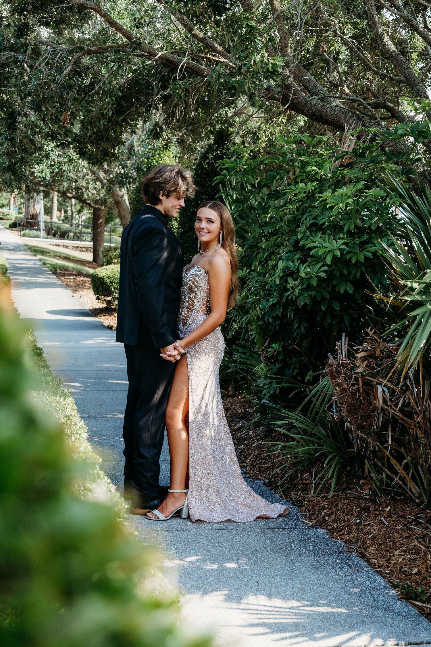 A romantic moment captured on a sunlit garden path surrounded by lush foliage.
