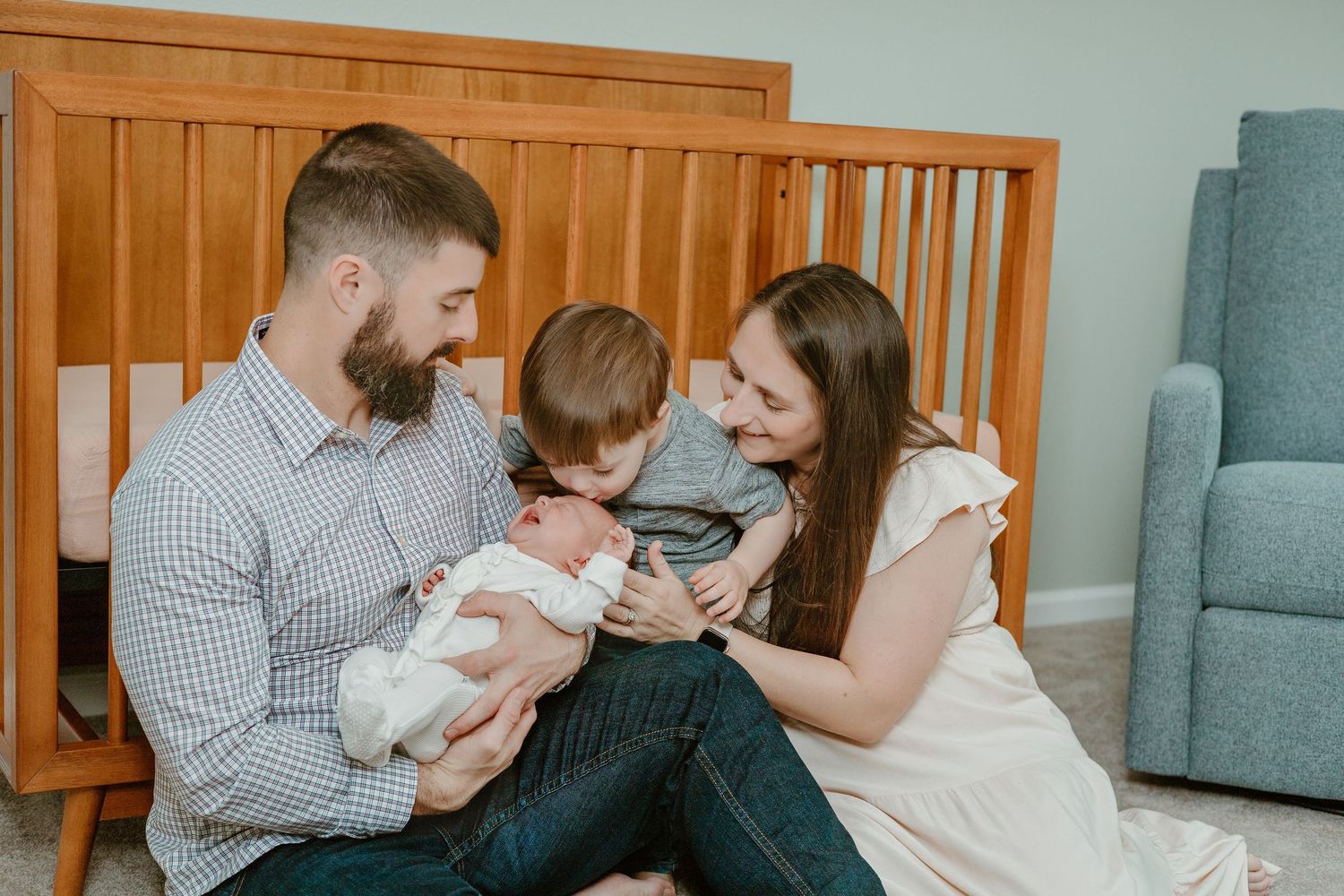 A family shares tender moments together on a gray couch with wooden furniture in the background.