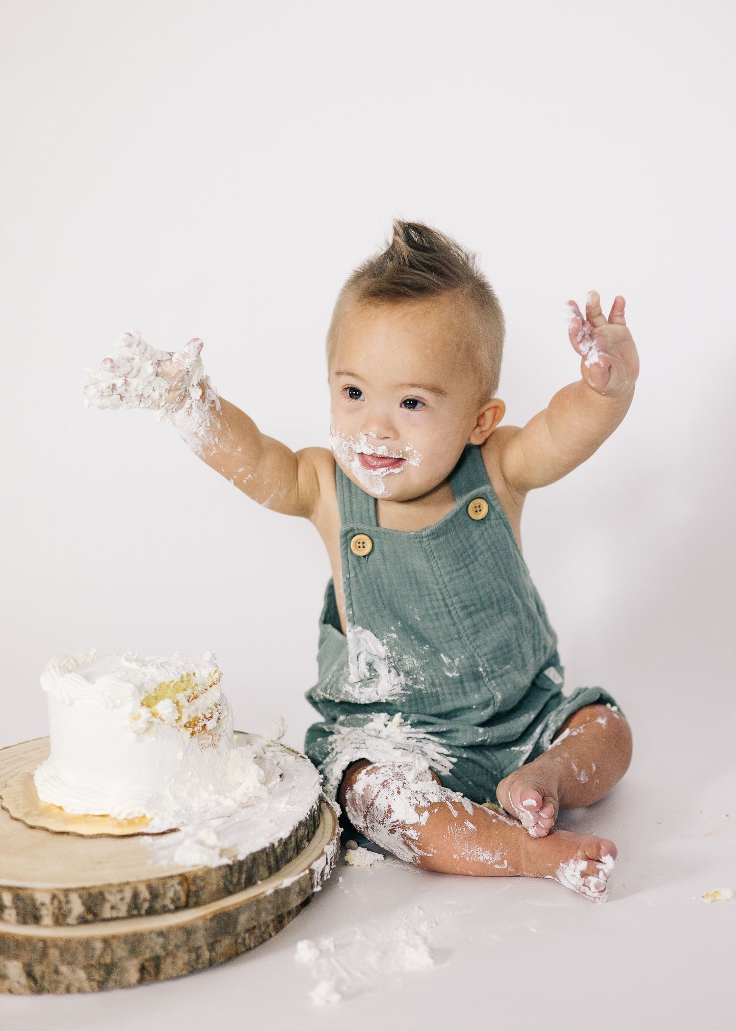 Baby in teal romper playing with cake and getting messy during cake smash photo session.