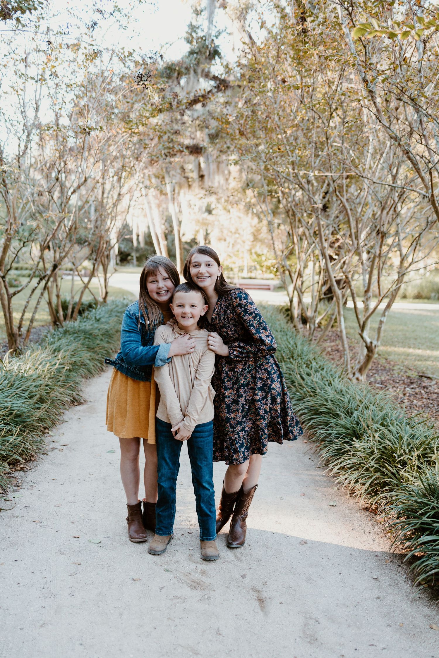 Three people stand together on a garden path surrounded by autumn foliage and ornamental grasses.