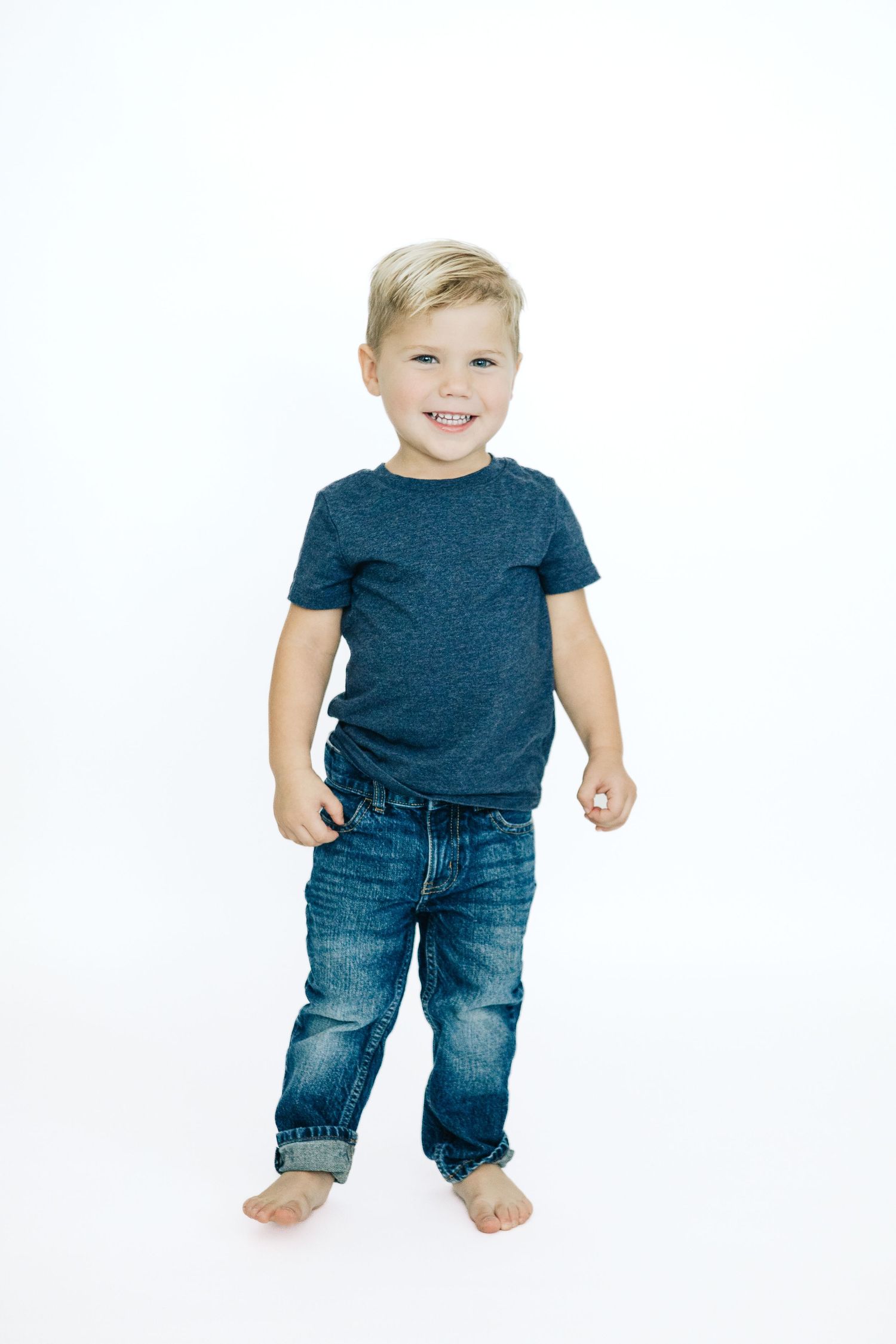 A toddler wearing blue jeans and a navy t-shirt stands against a white background in three different poses.