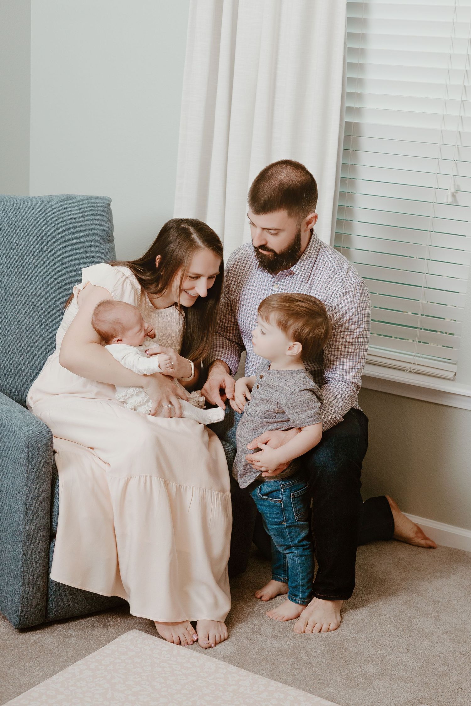 Family sitting together on grey couch sharing tender moments with children.