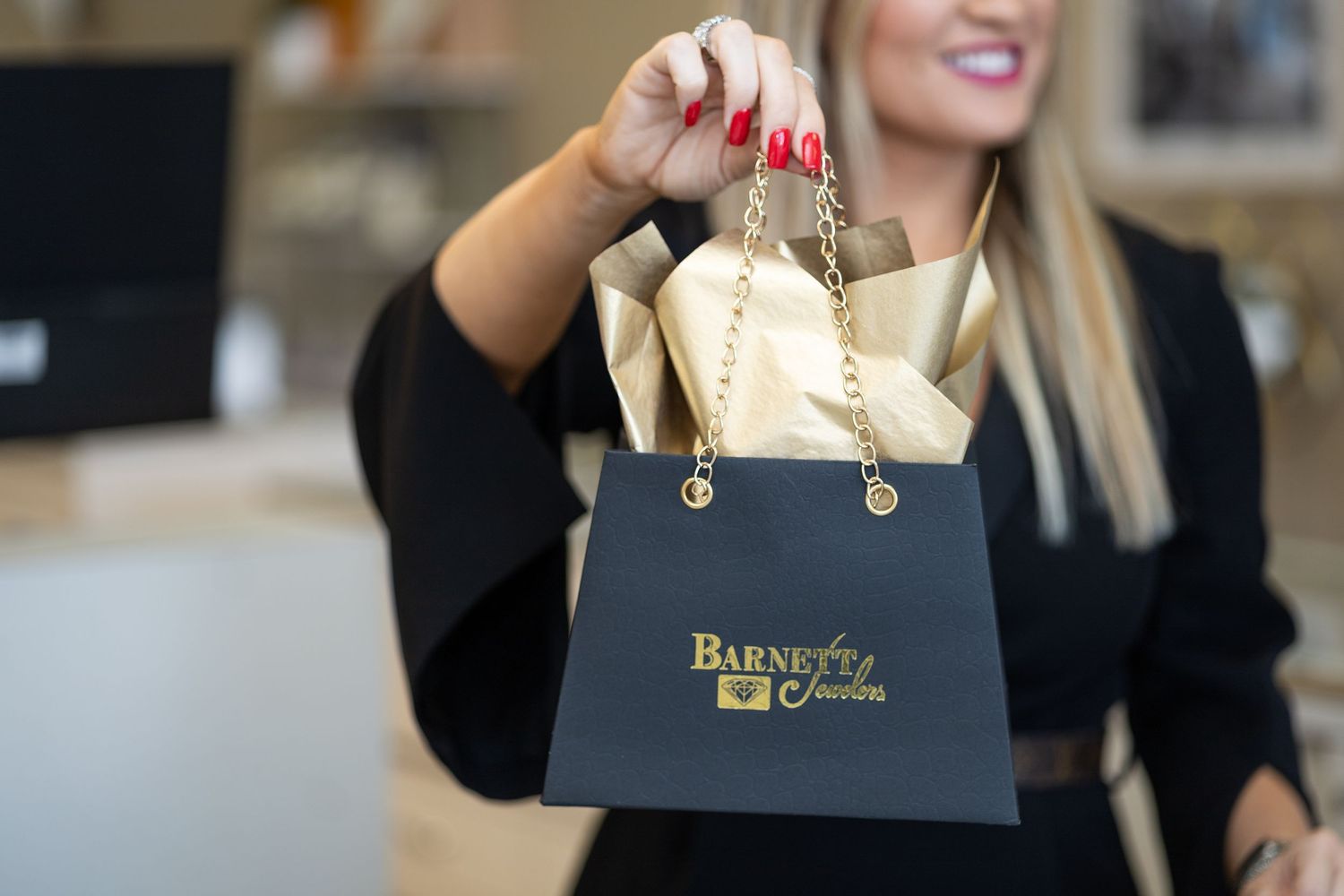 A person holds a black shopping bag with gold lettering in a retail store setting.