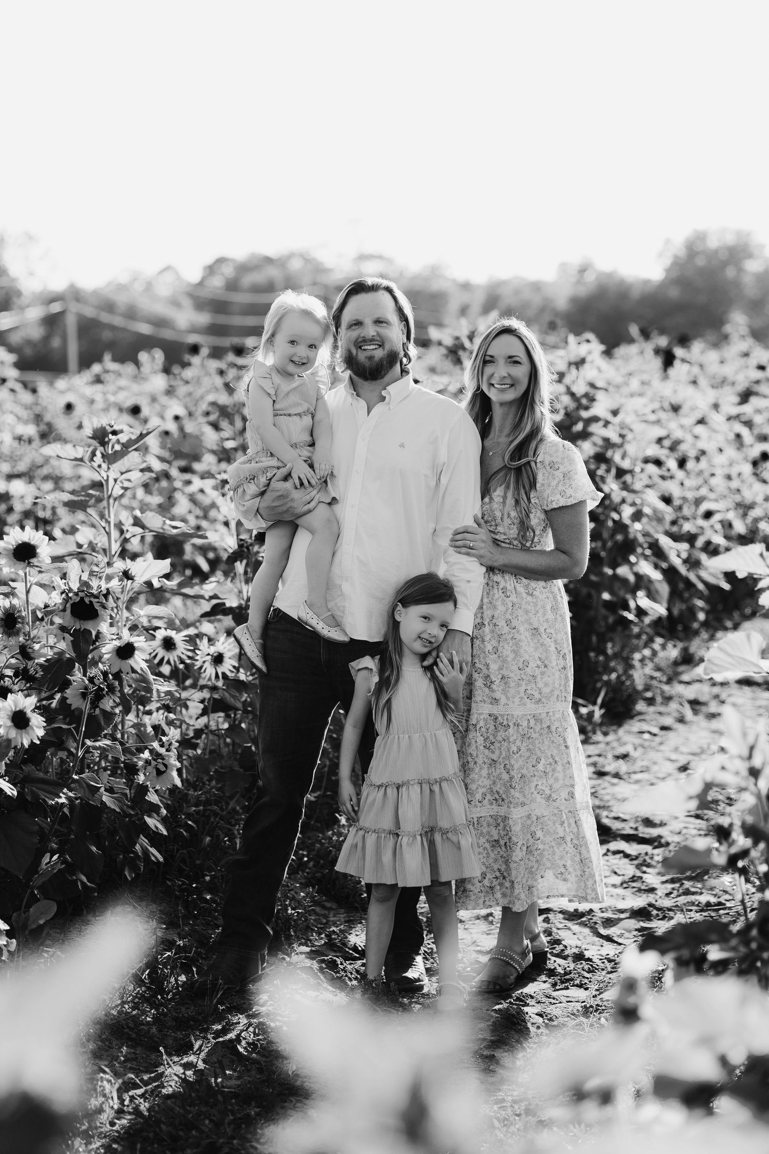 Black and white portrait of a family standing together in a flower field on a sunny day.