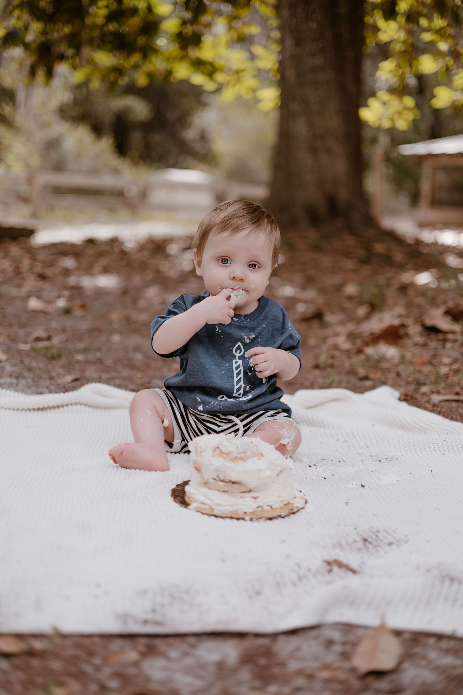 Baby sitting on white blanket outdoors enjoying cake smash session.