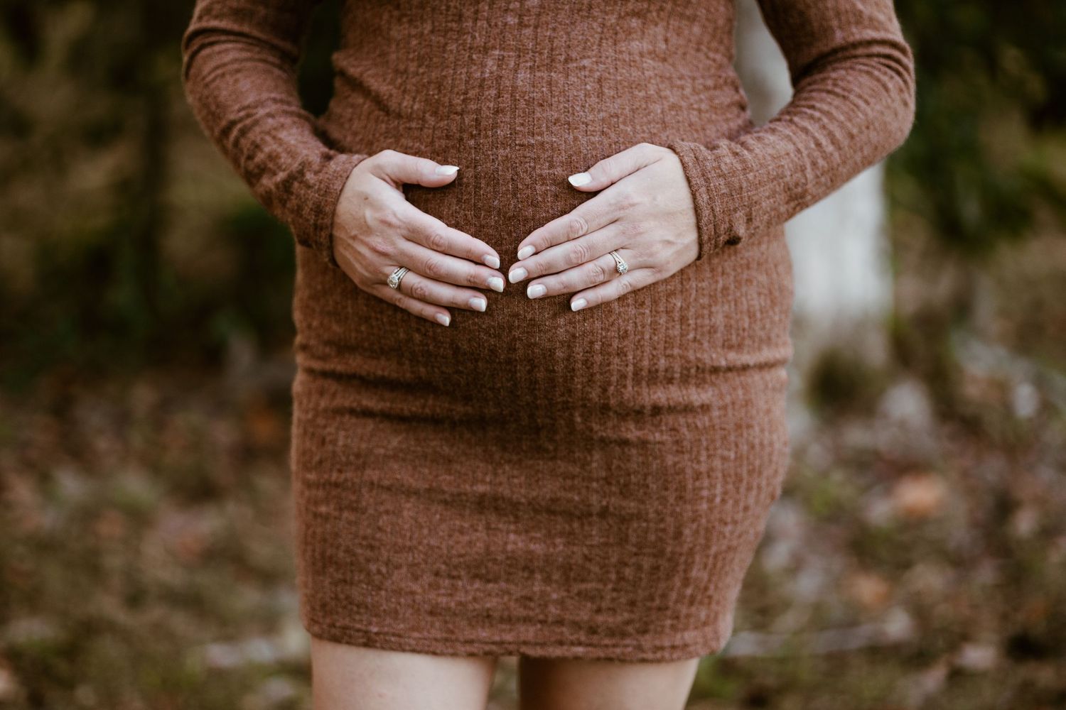 Person wearing brown sweater shown from torso down against dark background.