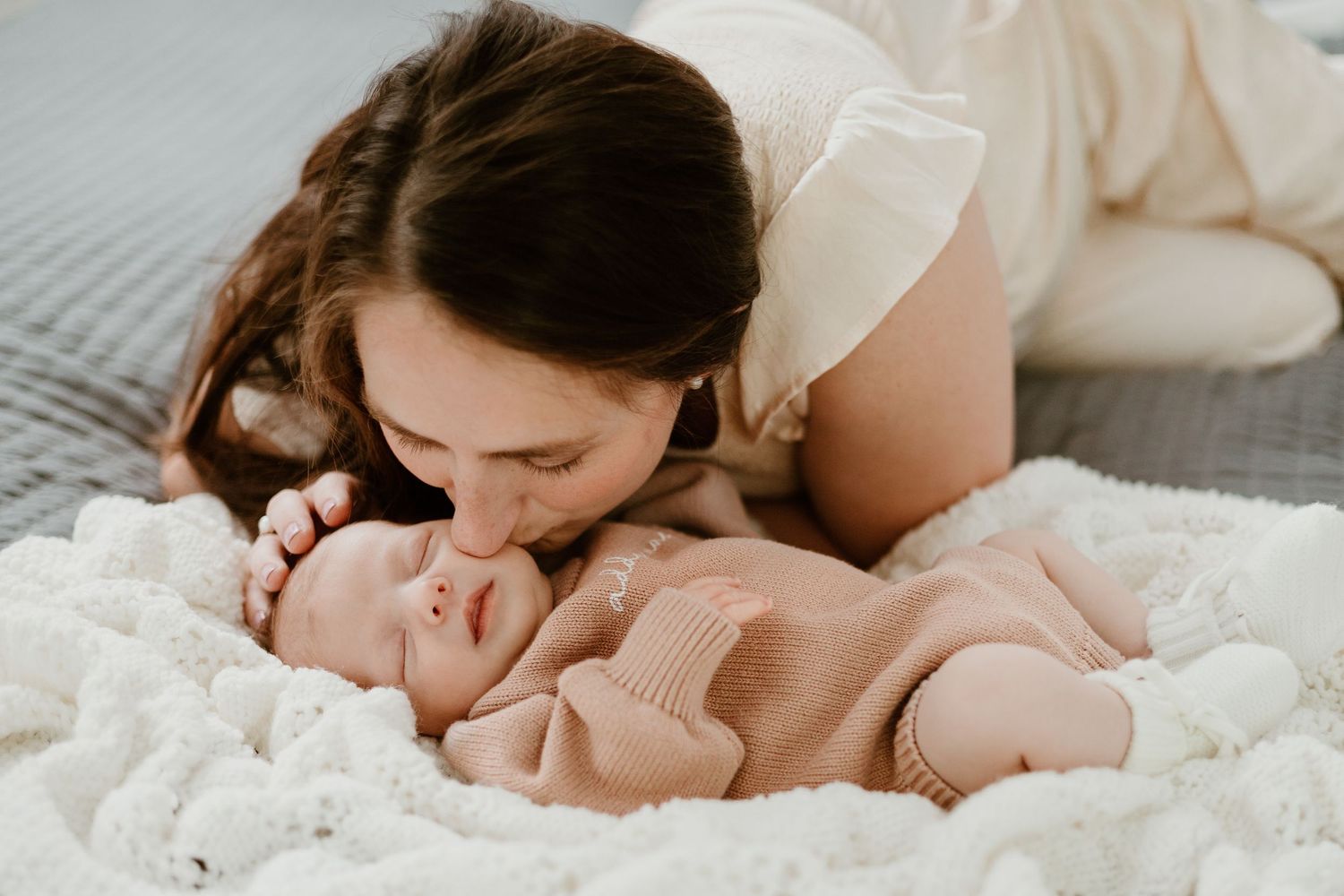 A tender moment captured as adults lean in close to a sleeping baby on white bedding.