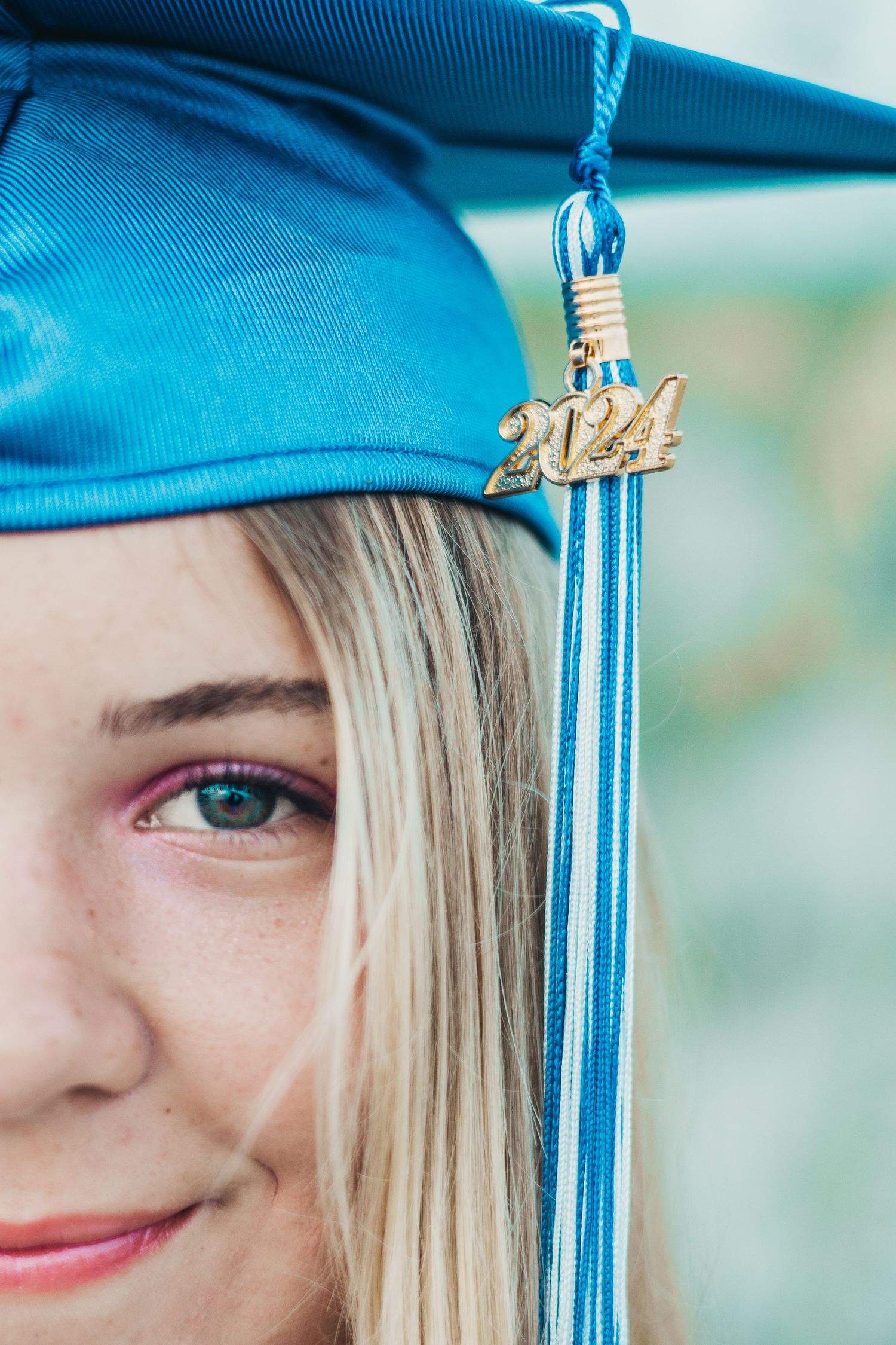Close-up of a bright blue graduation cap with 2024 tassel charm against a blurred background.