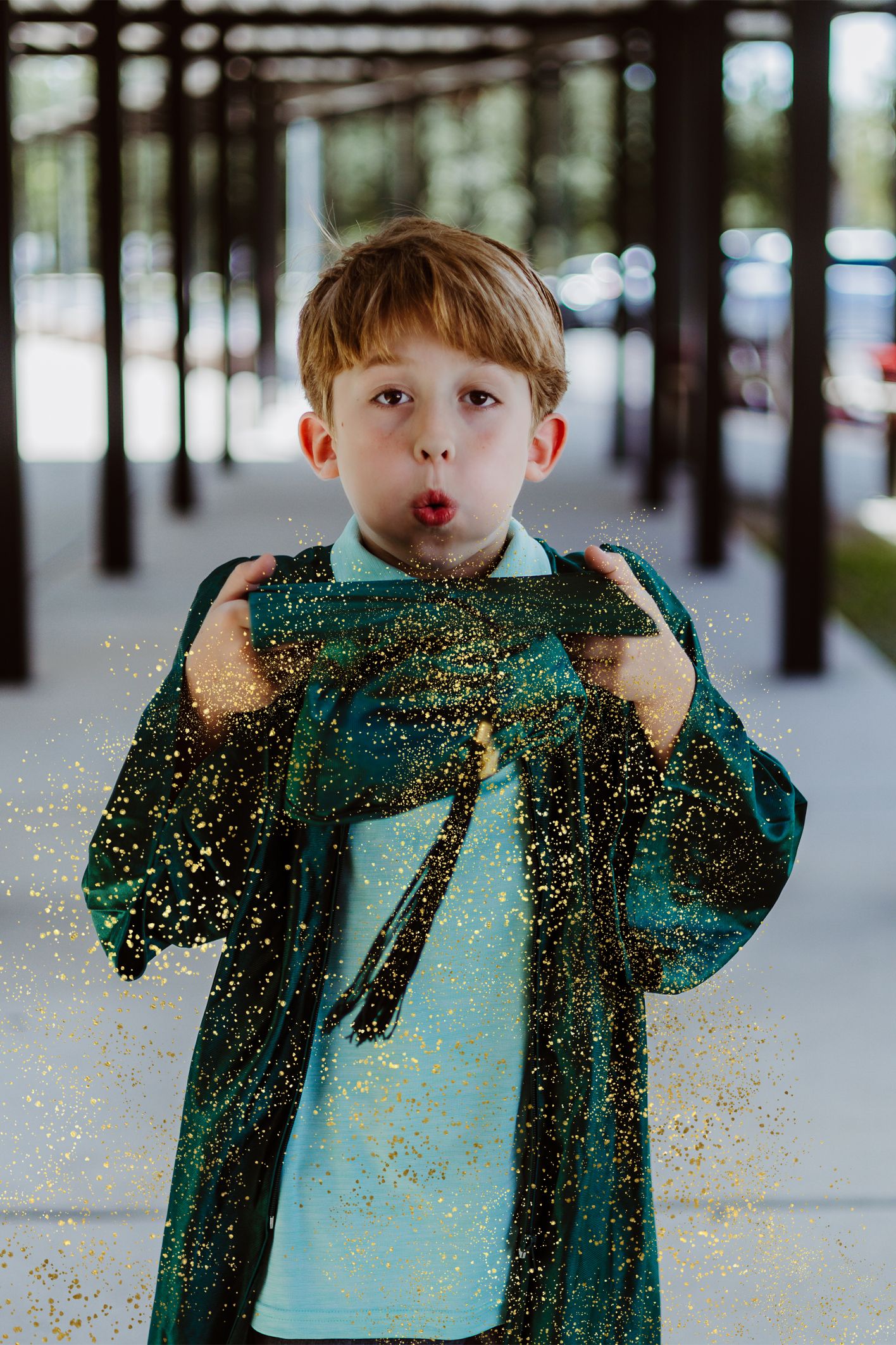Playful graduate in green cap and gown blowing glitter in sequence outdoors.