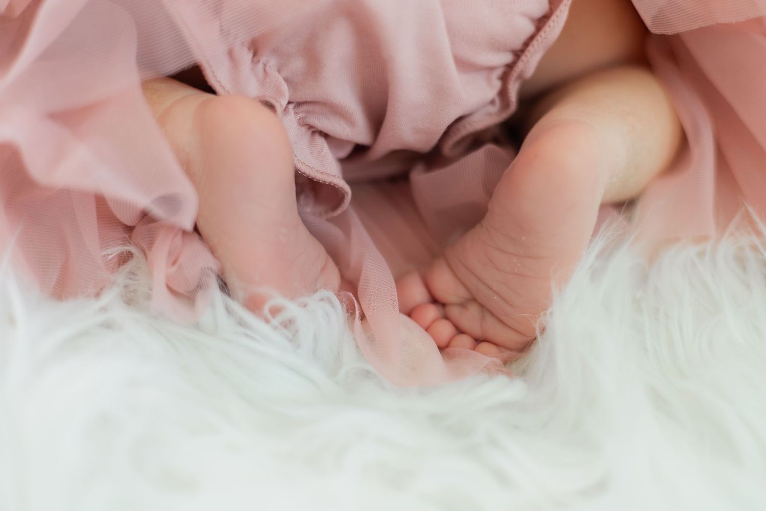 Artistic detail shot of pink tulle fabric and delicate newborn details on white fur.