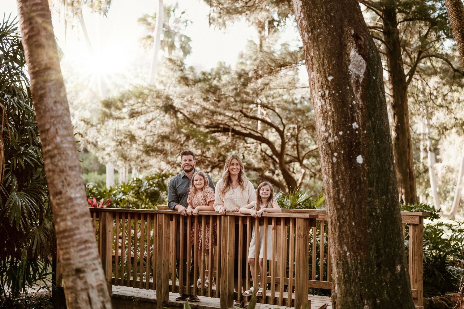 Family photo session on wooden deck with sunlight filtering through Spanish moss trees.