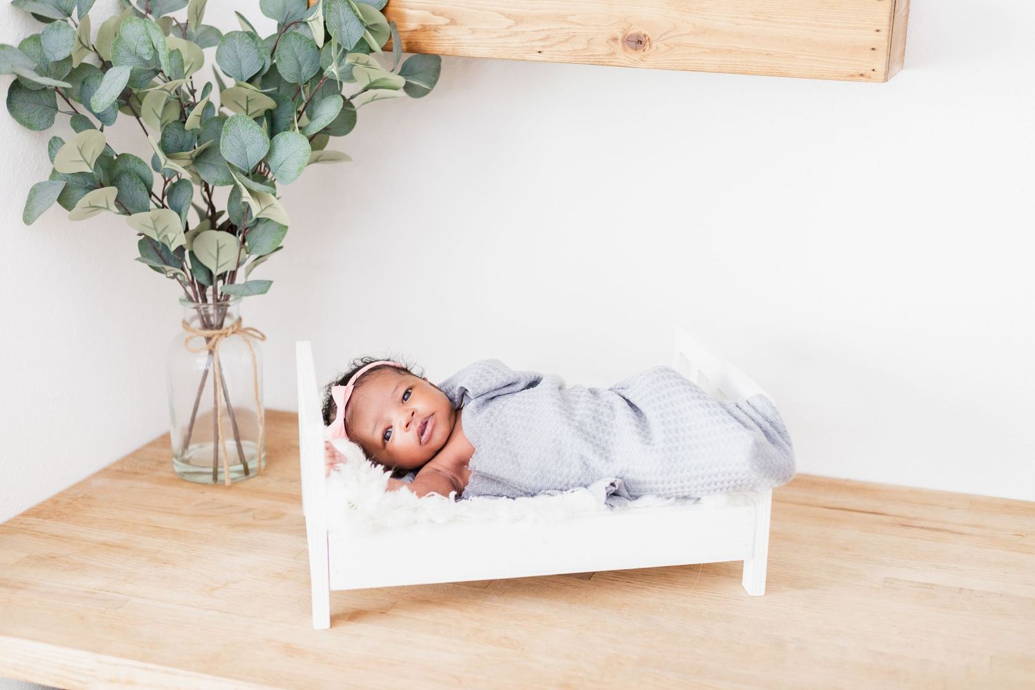 Nursery setting with wooden crib, eucalyptus decor, and white bedding.