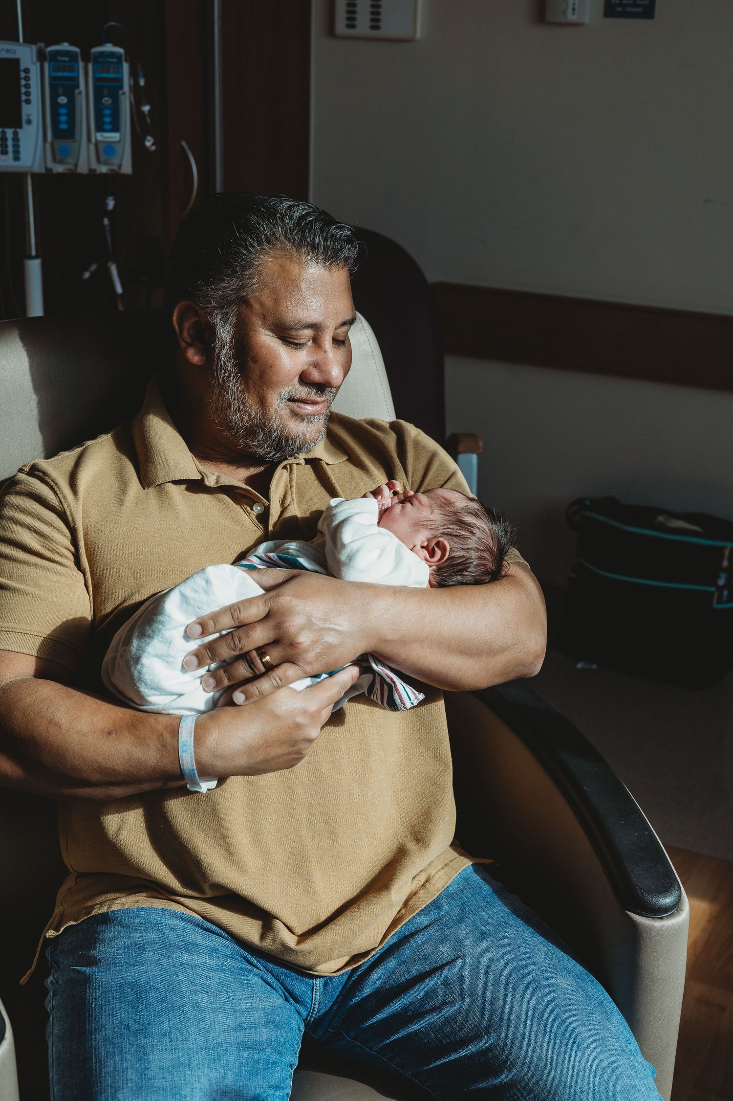 A person in a yellow shirt tenderly holding and feeding a swaddled infant.