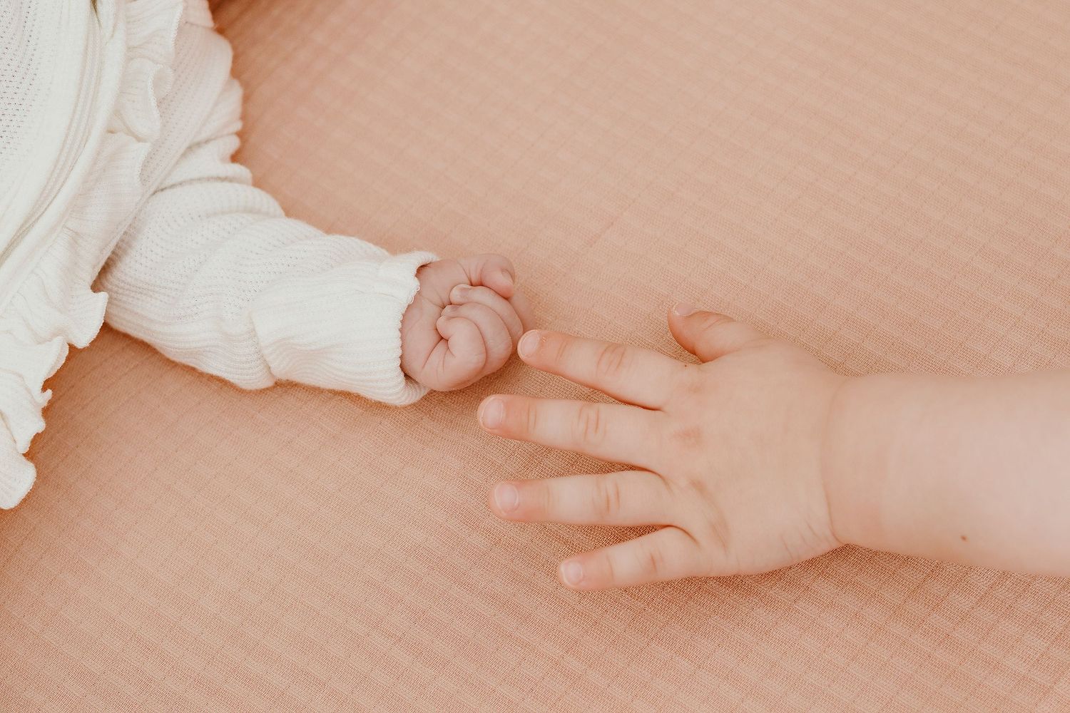 Close-up of baby's tiny hand against soft peach-colored background.