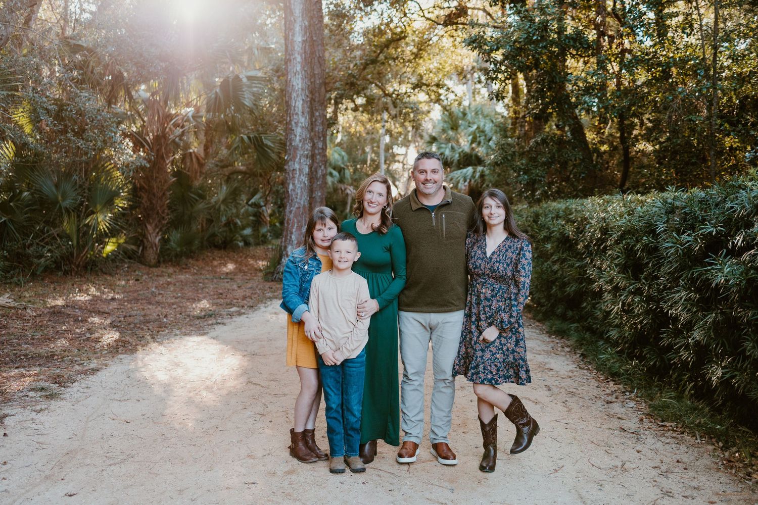 A group stands together on a sunlit dirt path surrounded by lush green foliage on an autumn afternoon.