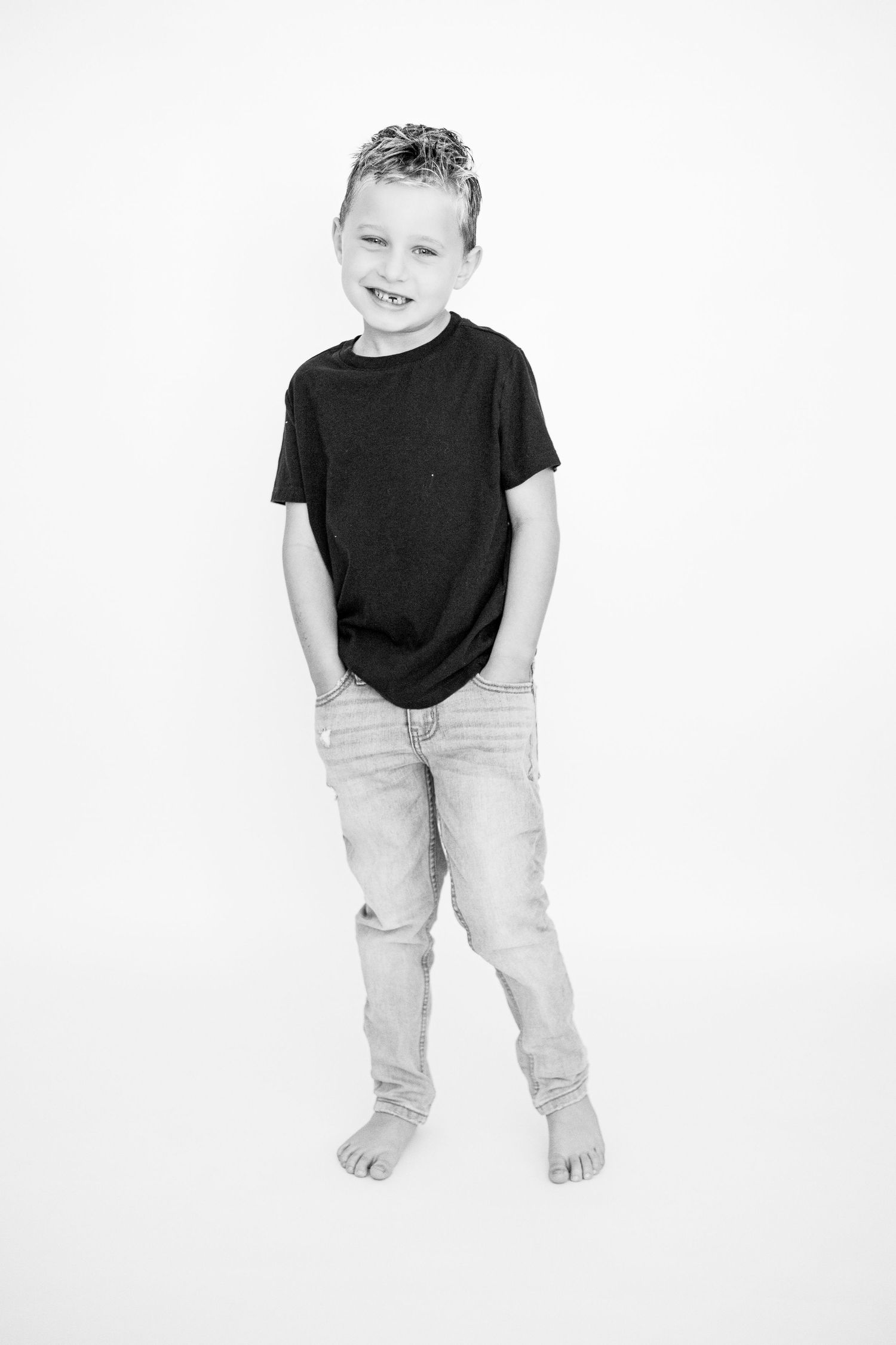 A child wearing a black t-shirt and light colored pants stands against a white background.